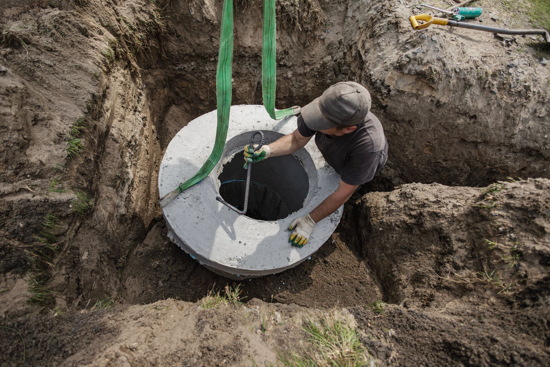 Worker lowers a concrete manhole ring into a trench with green straps. Worker lowers a concrete manhole ring into a trench with green straps.