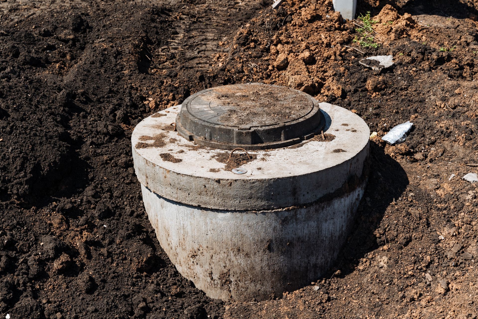 Concrete utility access cover in a dirt excavation site, with a round lid on top. Concrete utility access cover in a dirt excavation site, with a round lid on top.