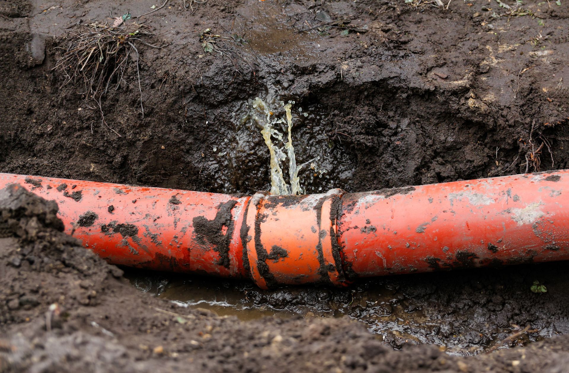 Broken orange pipe leaking water in a muddy trench Broken orange pipe leaking water in a muddy trench