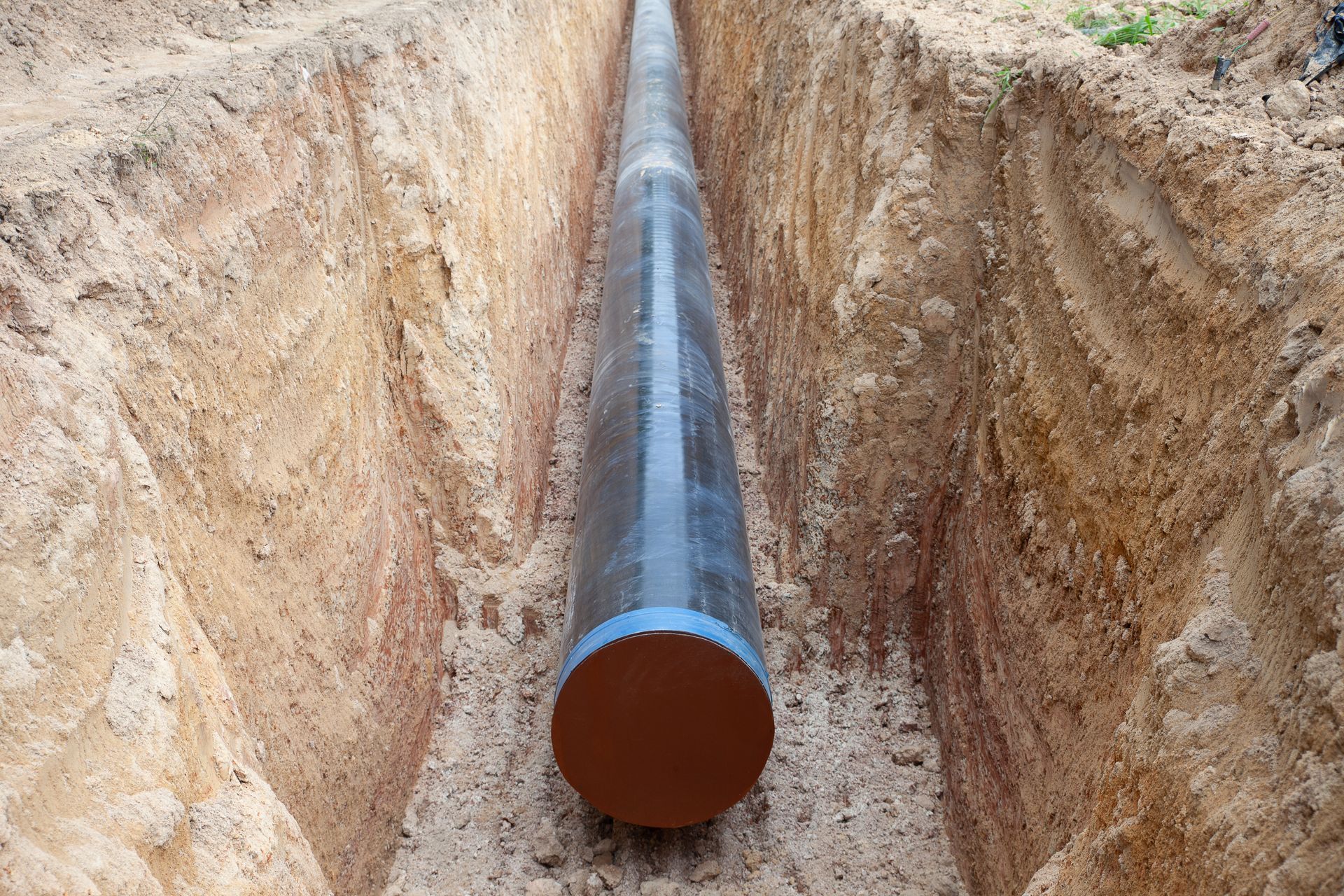 Long black pipeline laid in a narrow dirt trench, viewed from the open end. Long black pipeline laid in a narrow dirt trench, viewed from the open end.