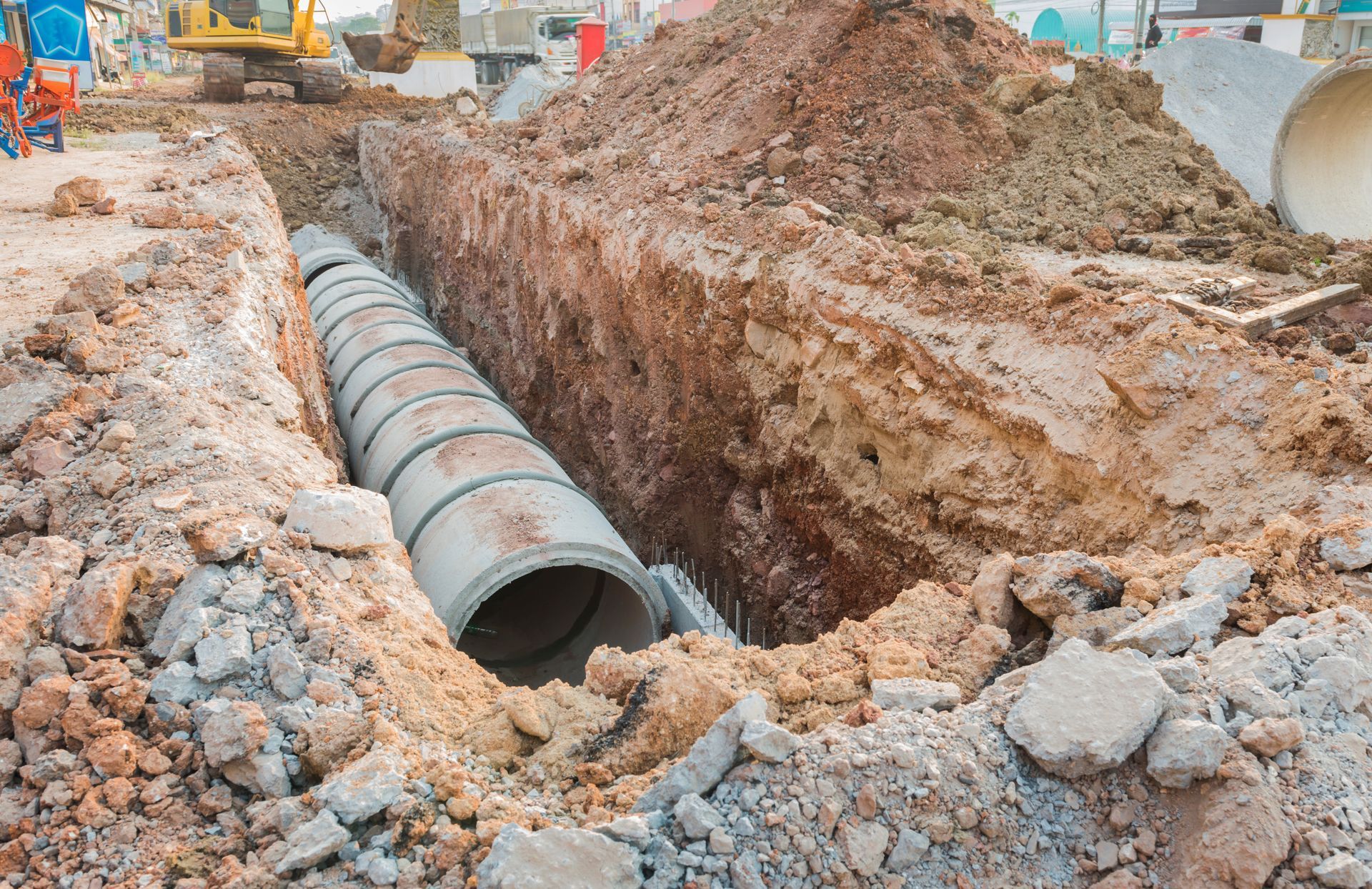 Workers installing a large concrete drainage pipe in a muddy trench at a construction site Workers installing a large concrete drainage pipe in a muddy trench at a construction site