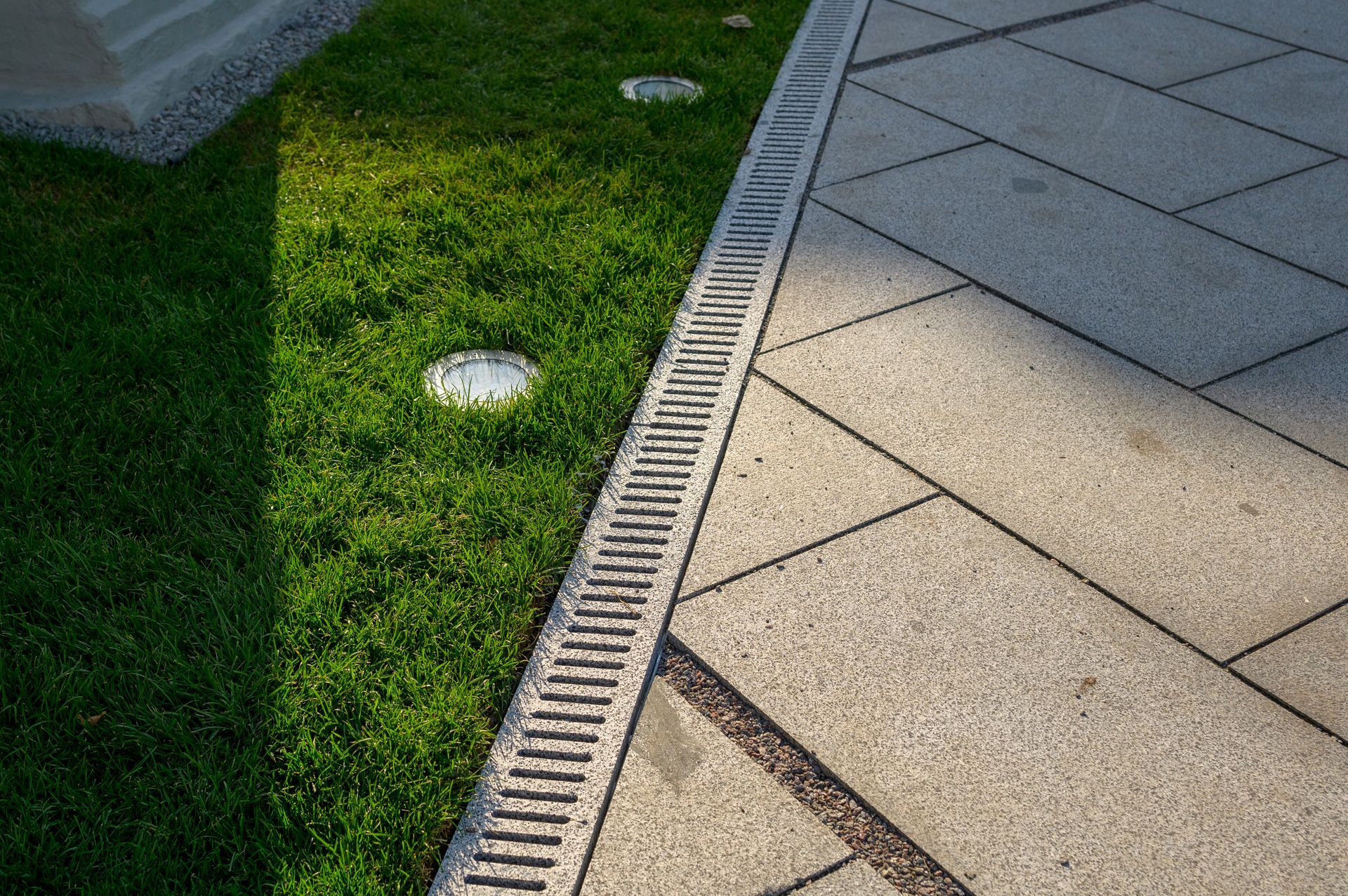 Grass lawn beside a paved walkway with a drainage grate and sunlight shadow Grass lawn beside a paved walkway with a drainage grate and sunlight shadow