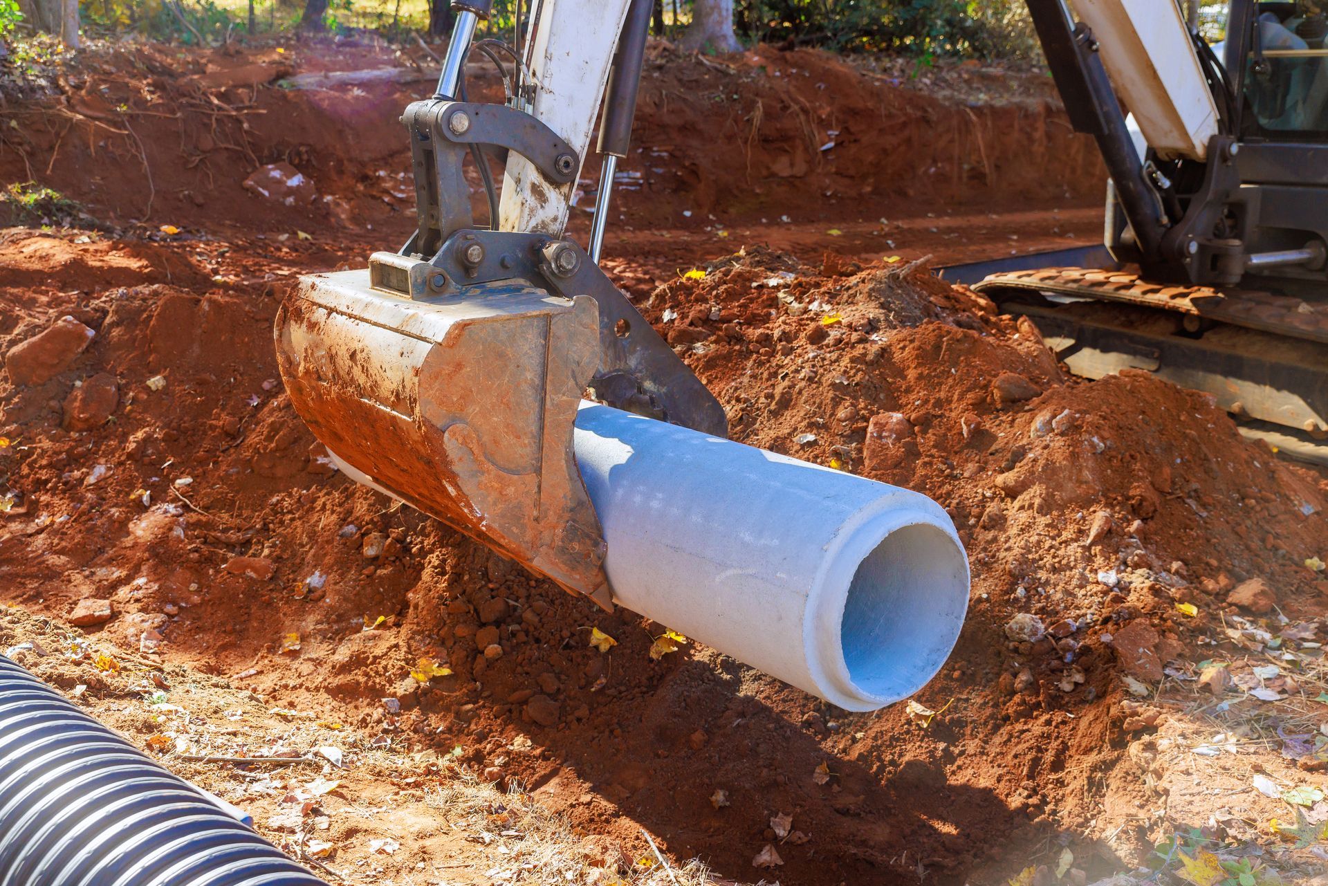 Excavator lowering a concrete pipe into a dirt trench at a construction site. Excavator lowering a concrete pipe into a dirt trench at a construction site.