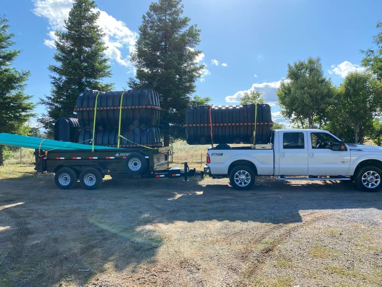 White pickup towing a trailer loaded with stacked black panels in a gravel lot under a blue sky White pickup towing a trailer loaded with stacked black panels in a gravel lot under a blue sky