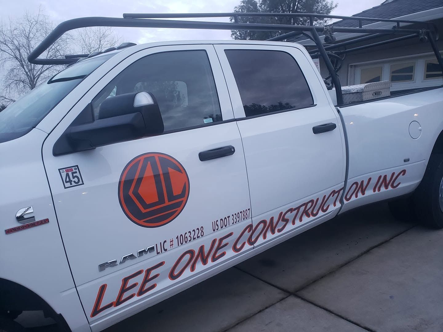 White Lee One Construction pickup truck parked in a driveway, with company logo and red lettering on the door White Lee One Construction pickup truck parked in a driveway, with company logo and red lettering on the door