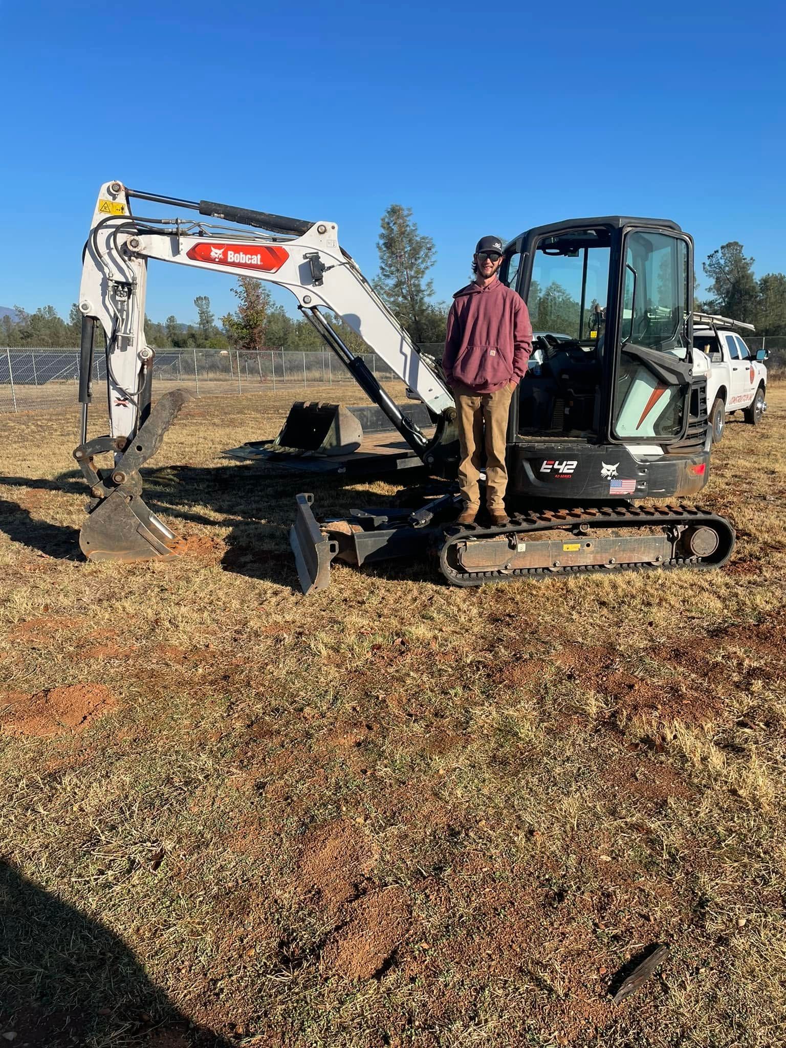 Mini excavator and worker raking leaves in a grassy field on a sunny day. Mini excavator and worker raking leaves in a grassy field on a sunny day.