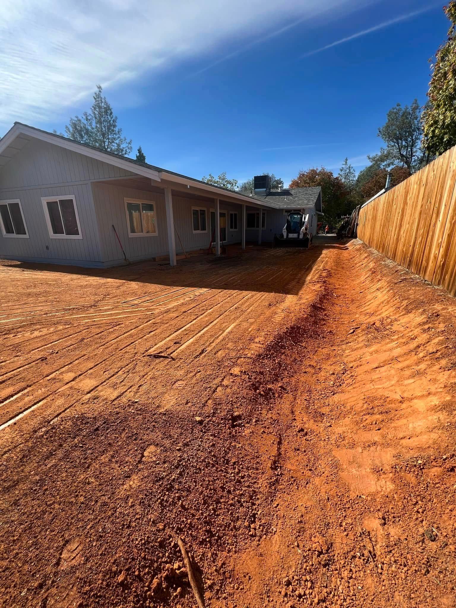 Red dirt driveway beside a beige house and wooden fence under a bright blue sky Red dirt driveway beside a beige house and wooden fence under a bright blue sky