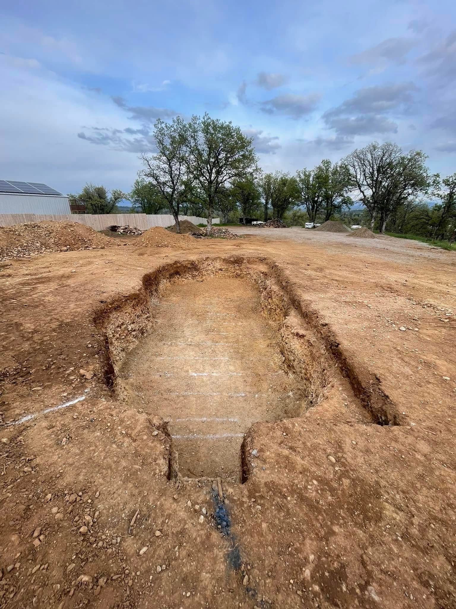 Excavation trench cut into a dirt field under a cloudy sky, with trees in the background Excavation trench cut into a dirt field under a cloudy sky, with trees in the background