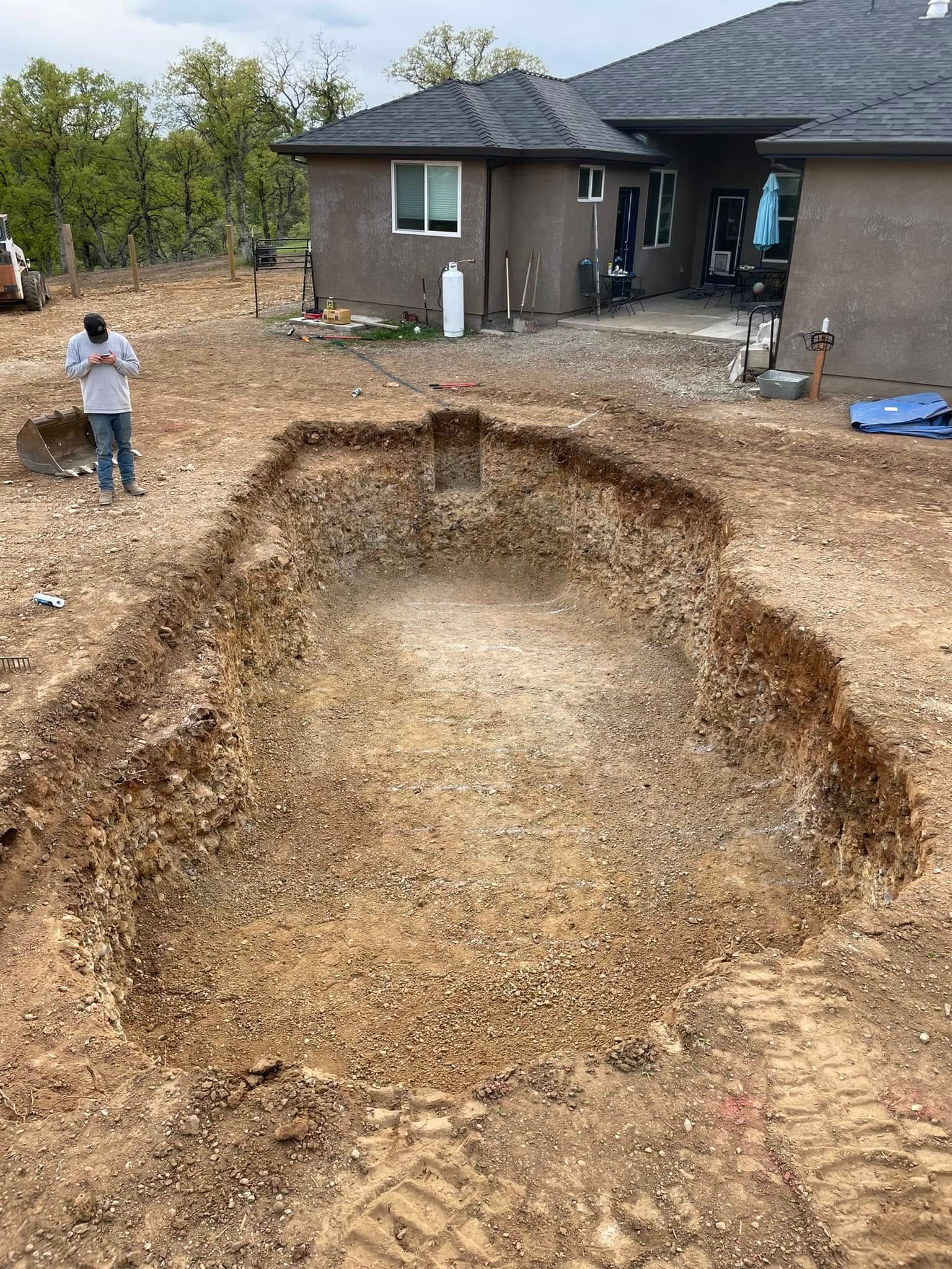 Large dug-out dirt pit in a yard near a house, with a person standing to the left. Large dug-out dirt pit in a yard near a house, with a person standing to the left.