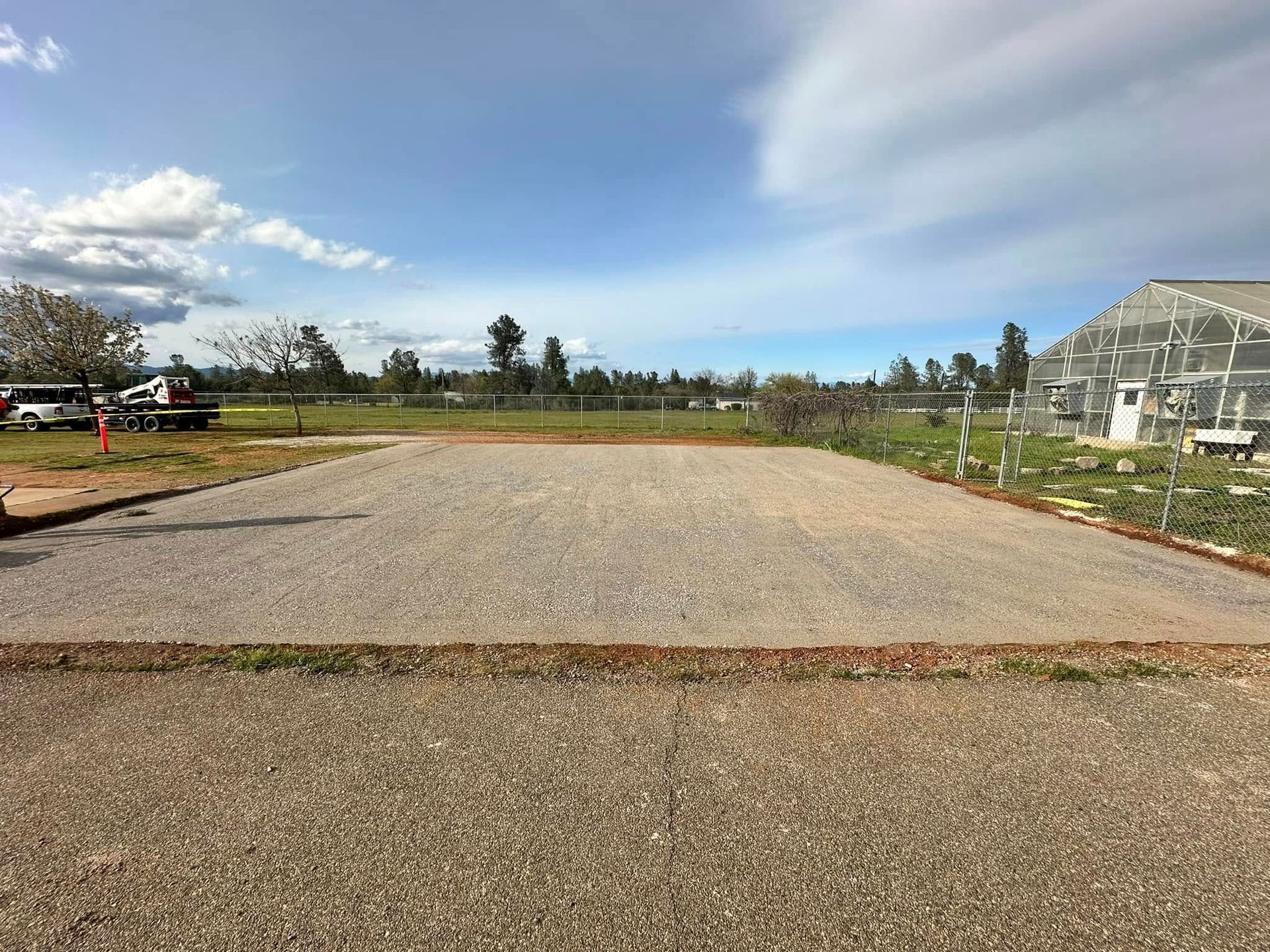 Gravel parking lot under construction beside a greenhouse, with open sky and a worker in the distance Gravel parking lot under construction beside a greenhouse, with open sky and a worker in the distance