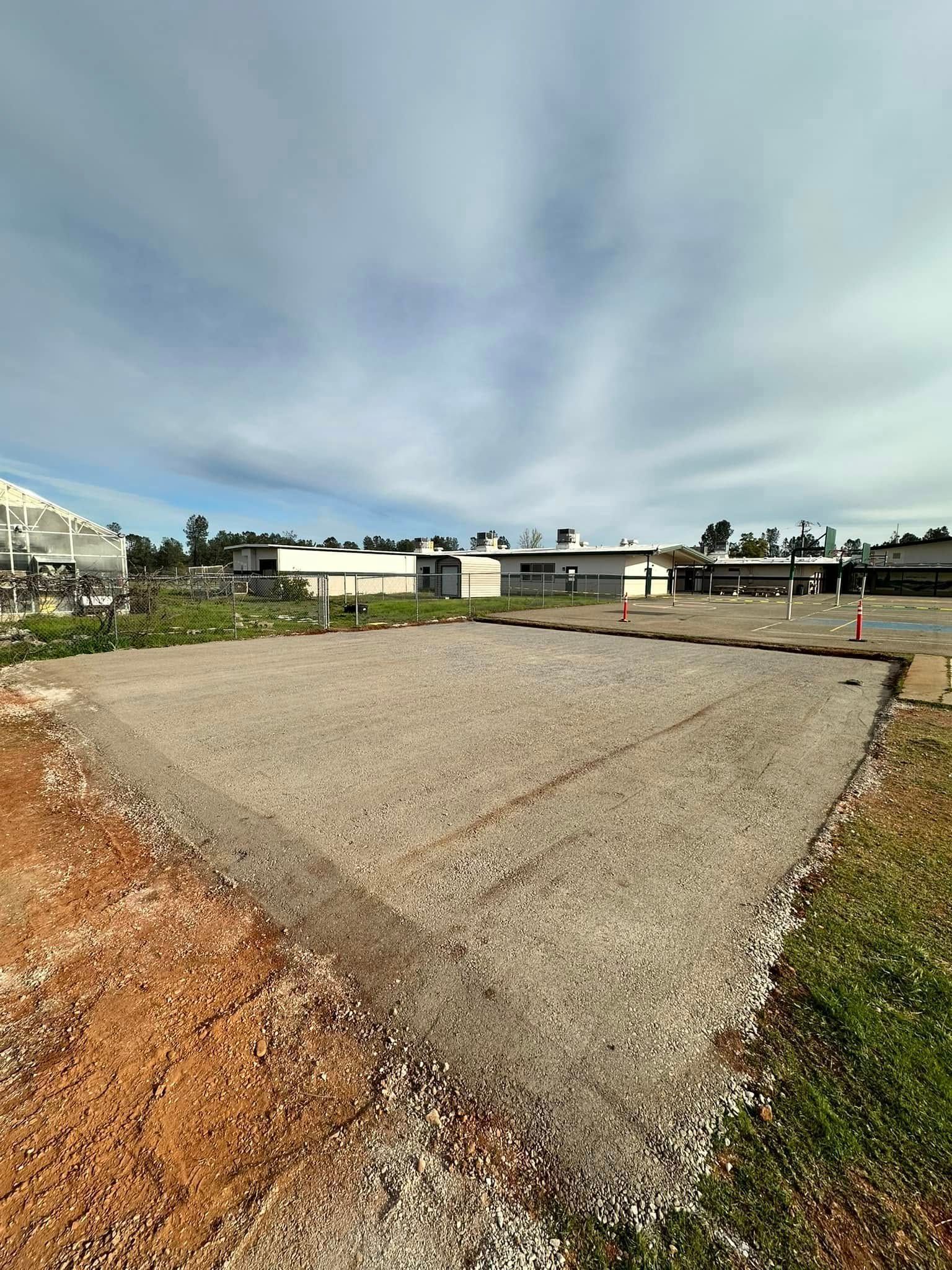 Wide gravel lot beside buildings under a cloudy sky with red dirt and grass edges Wide gravel lot beside buildings under a cloudy sky with red dirt and grass edges