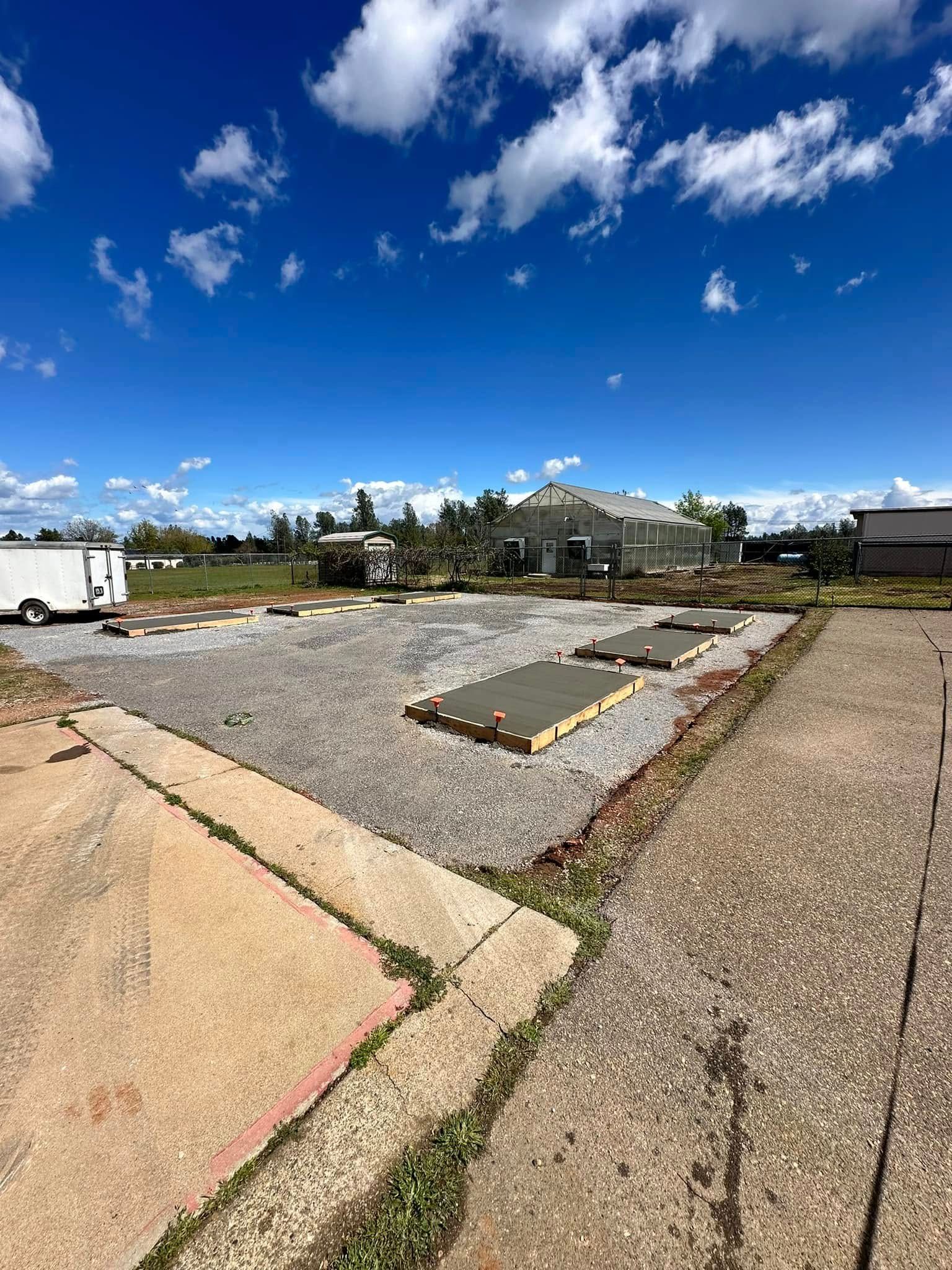 Empty gravel lot under a bright blue sky with scattered clouds, bordered by sidewalks and low buildings. Empty gravel lot under a bright blue sky with scattered clouds, bordered by sidewalks and low buildings.