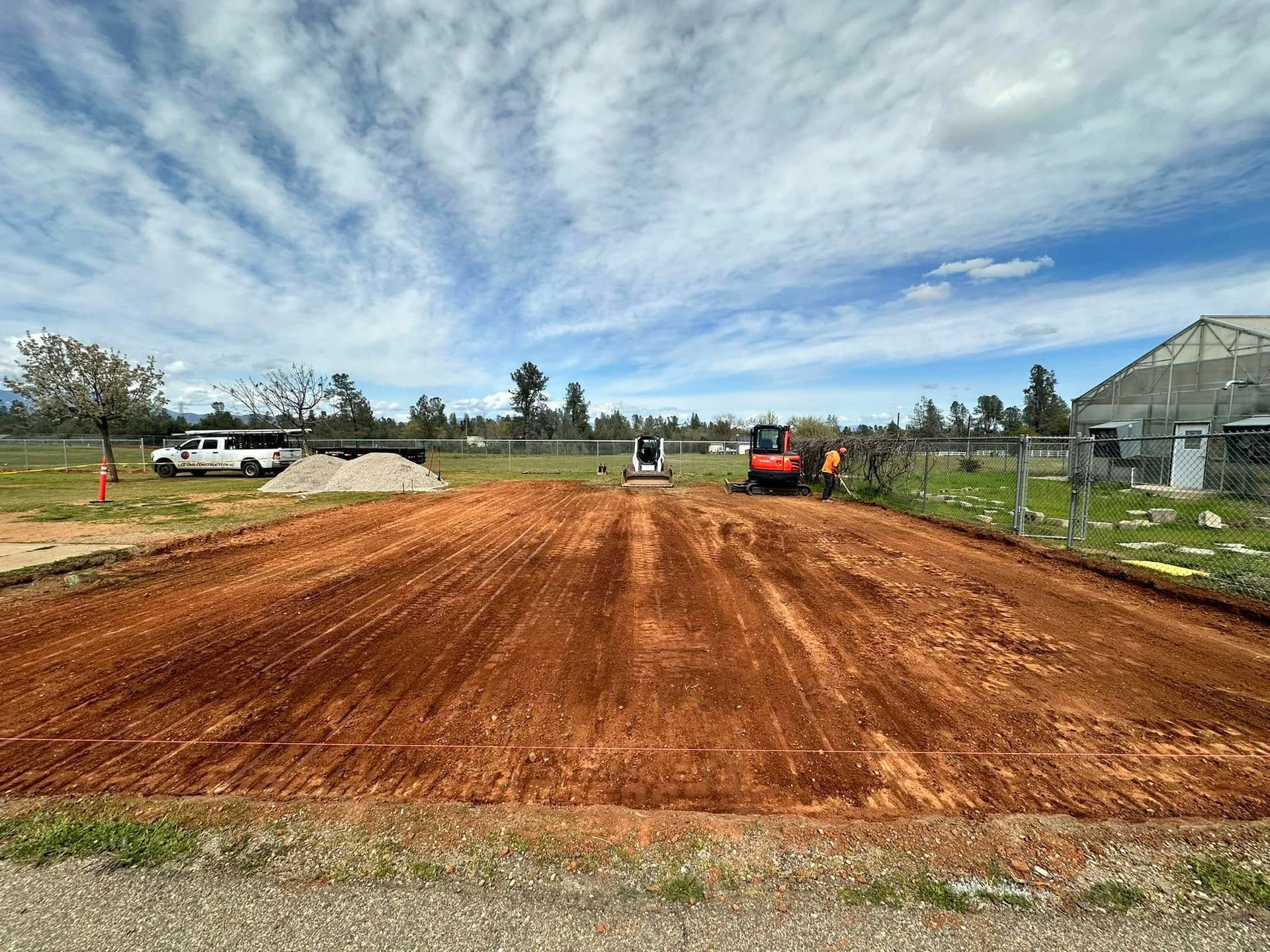 Freshly graded red dirt lot beside a greenhouse under a cloudy sky Freshly graded red dirt lot beside a greenhouse under a cloudy sky