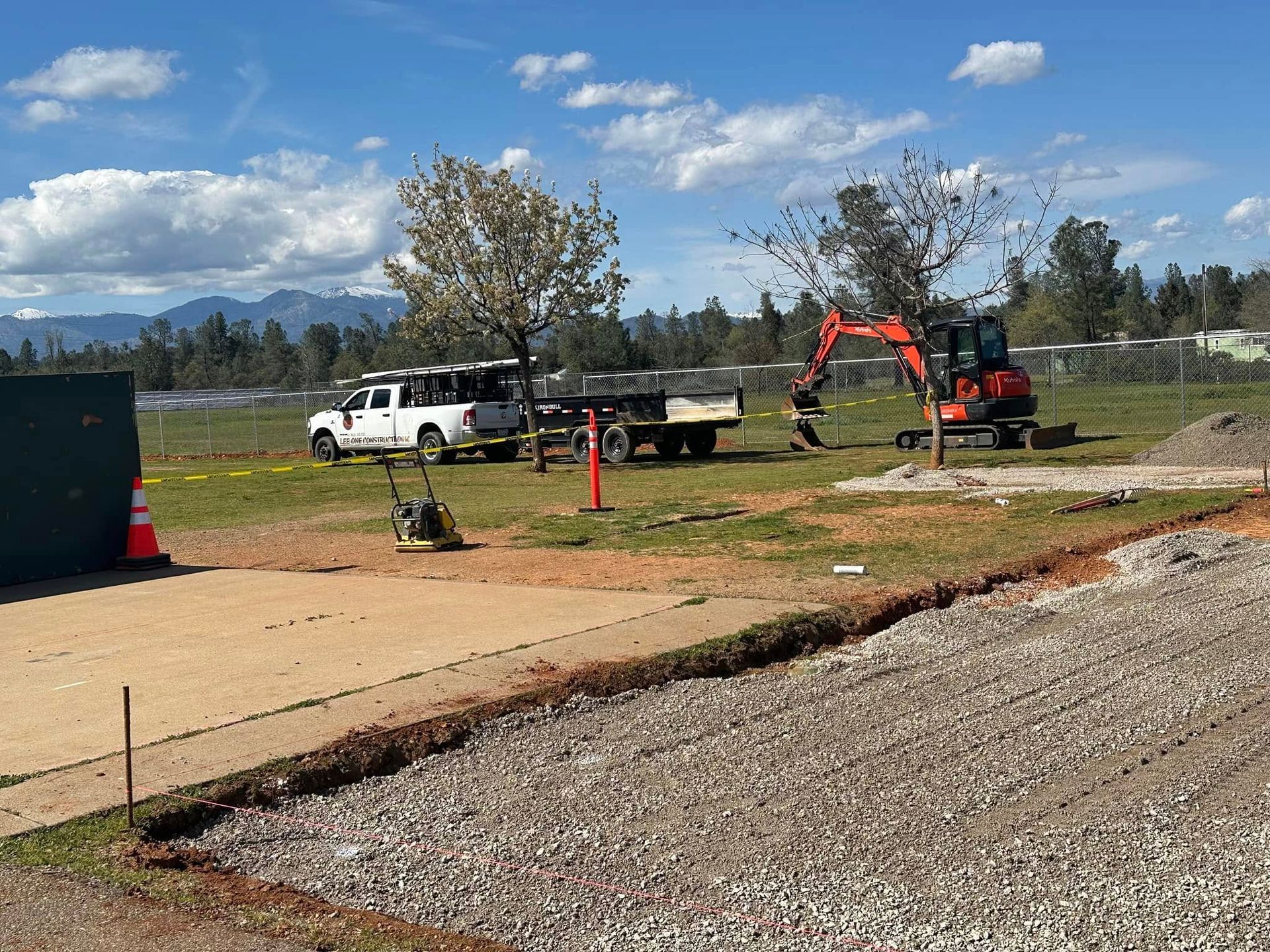 Construction site with a white truck and orange excavator on a grassy field under a blue sky Construction site with a white truck and orange excavator on a grassy field under a blue sky
