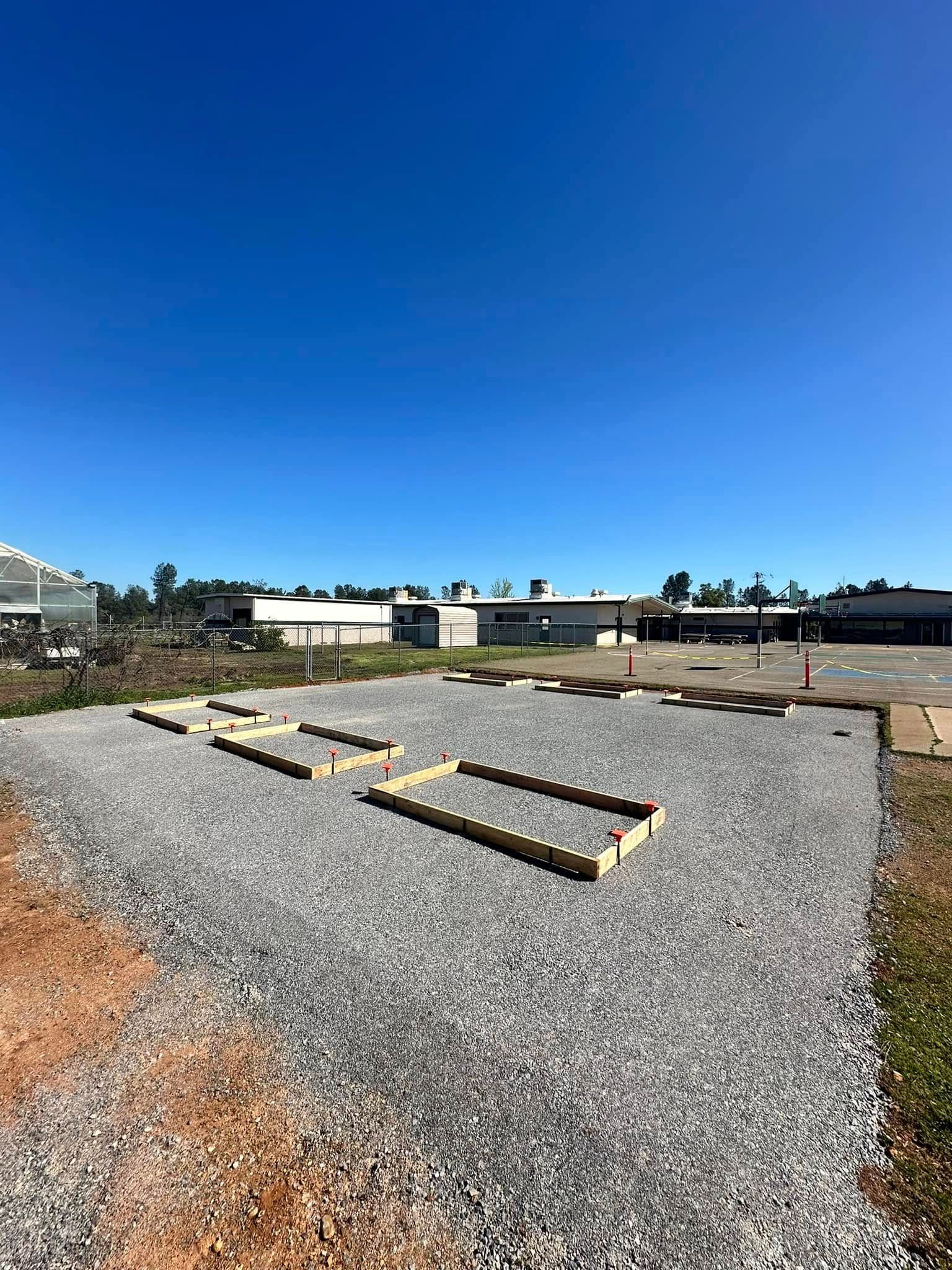 Gravel lot with several raised wooden planting beds under a clear blue sky. Gravel lot with several raised wooden planting beds under a clear blue sky.