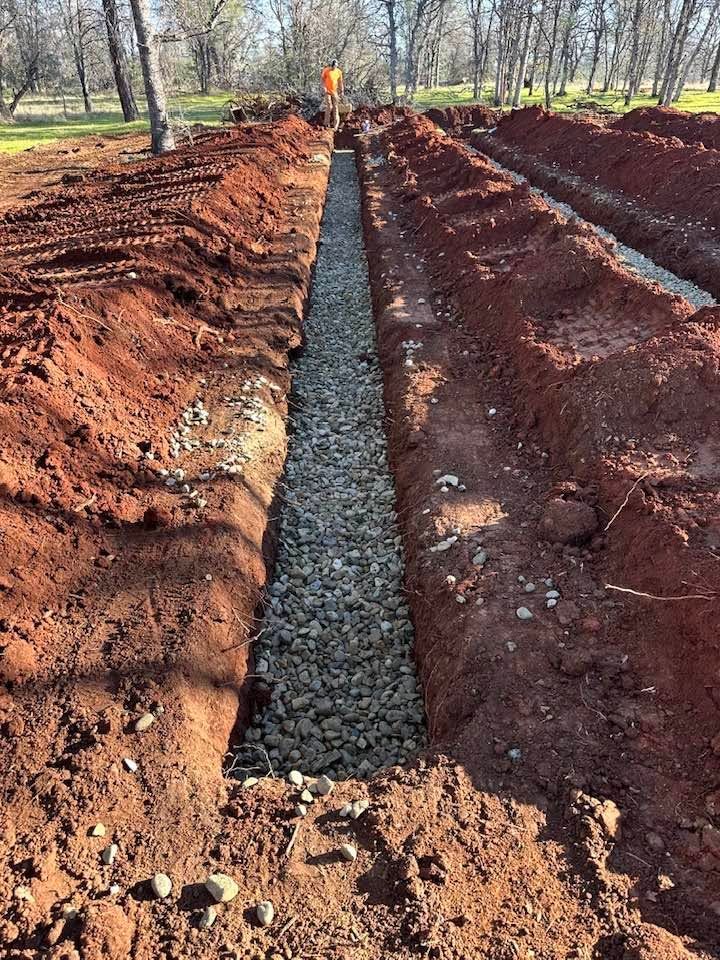 Freshly dug trench filled with gravel between red soil banks in a wooded area Freshly dug trench filled with gravel between red soil banks in a wooded area