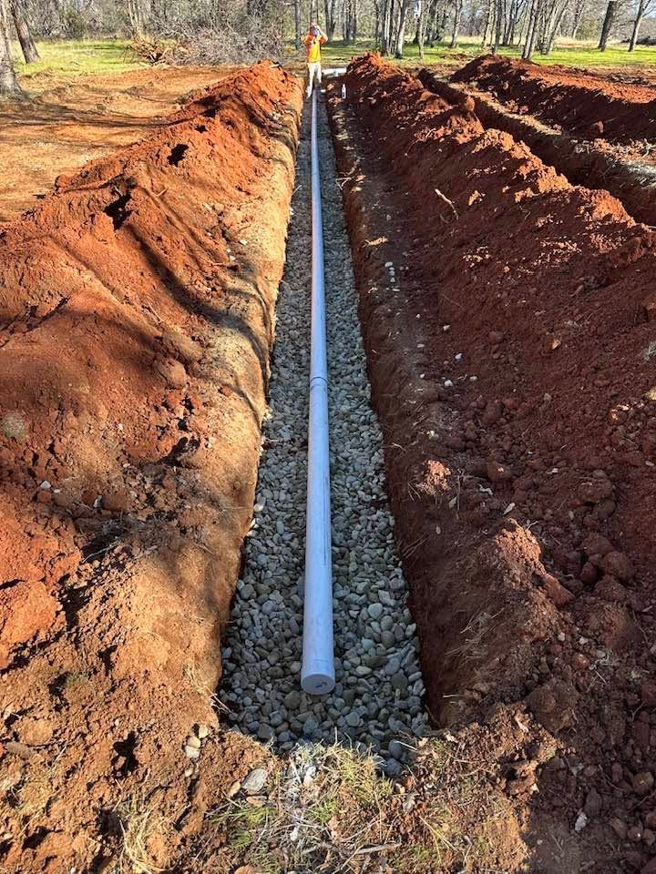 Trenched ditch with a white PVC pipe laid in gravel between mounds of red dirt outdoors Trenched ditch with a white PVC pipe laid in gravel between mounds of red dirt outdoors