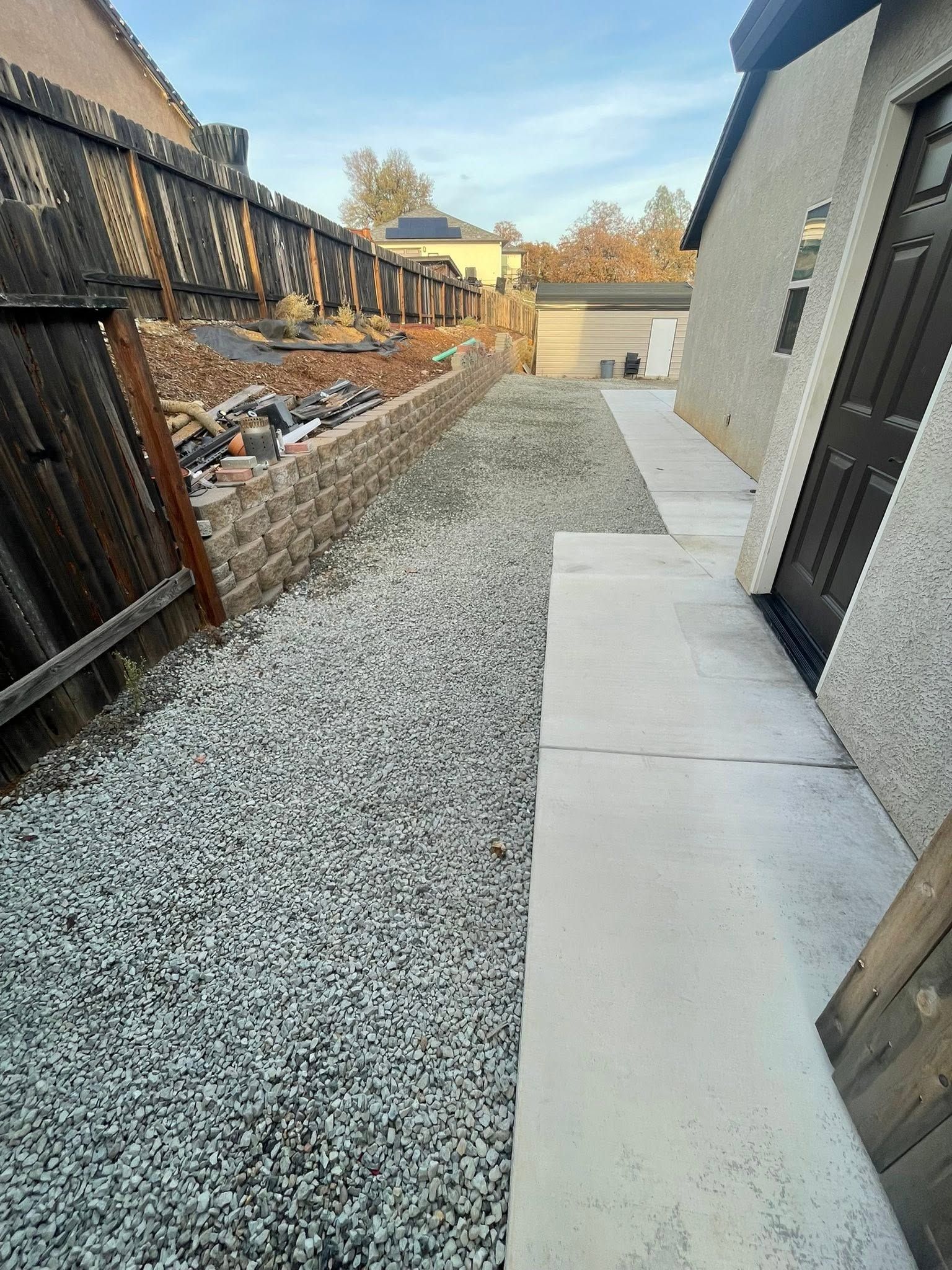 Narrow gravel side yard with concrete path beside a gray house and wooden fence. Narrow gravel side yard with concrete path beside a gray house and wooden fence.