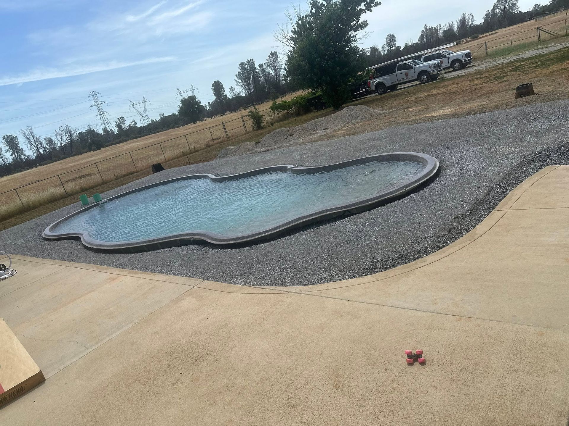 Backyard swimming pool with a stone border and concrete patio, set in a dry rural yard. Backyard swimming pool with a stone border and concrete patio, set in a dry rural yard.