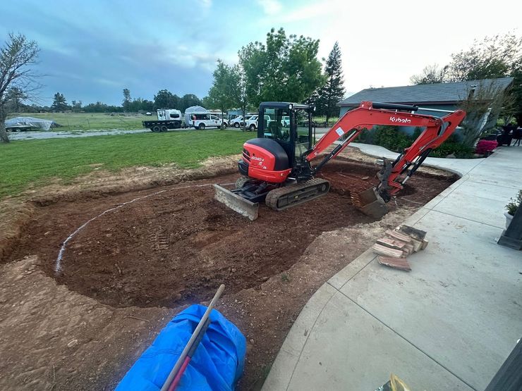 Red mini excavator grading a dirt area beside a driveway and house Red mini excavator grading a dirt area beside a driveway and house
