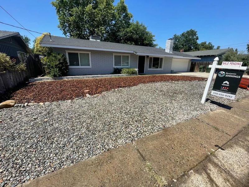 Single-story gray house with gravel front yard and for-sale sign by the sidewalk Single-story gray house with gravel front yard and for-sale sign by the sidewalk