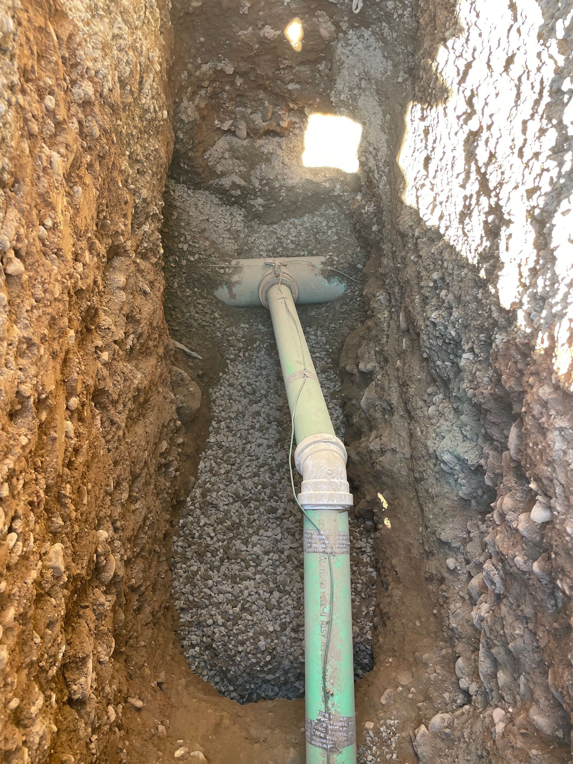Narrow trench with exposed green and white pipe running through dirt walls Narrow trench with exposed green and white pipe running through dirt walls