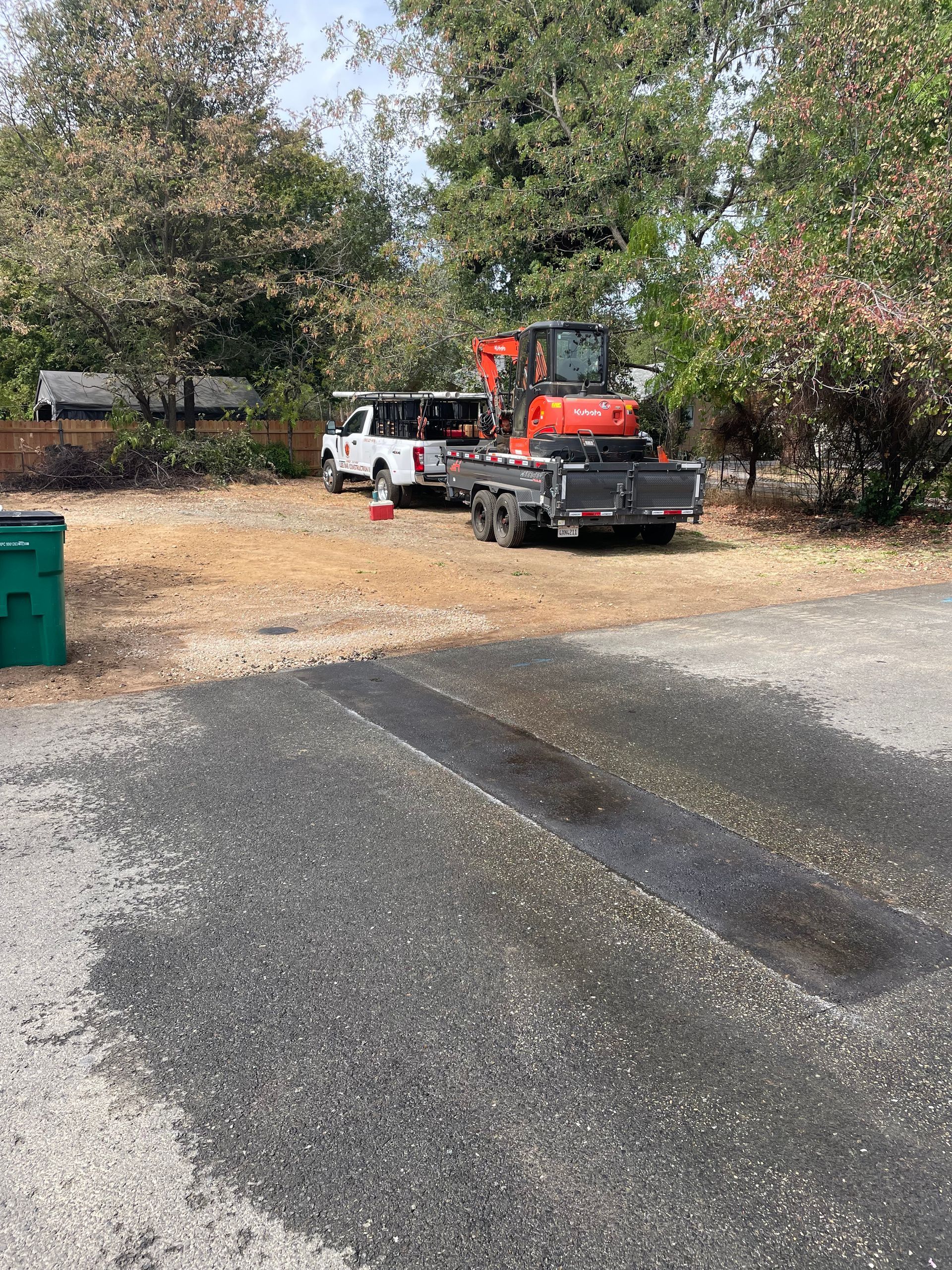 Orange excavator on a flatbed truck parked on a gravel driveway near trees and a road. Orange excavator on a flatbed truck parked on a gravel driveway near trees and a road.