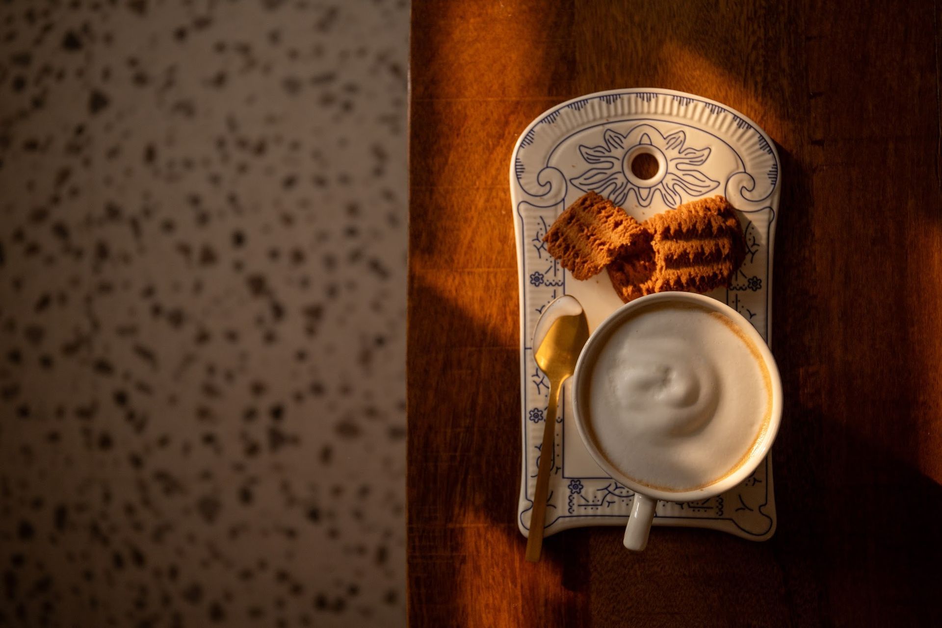 Koffiekopje op een schoteltje naast een papieren tas met patroon op een houten tafel in het warme zonlicht.