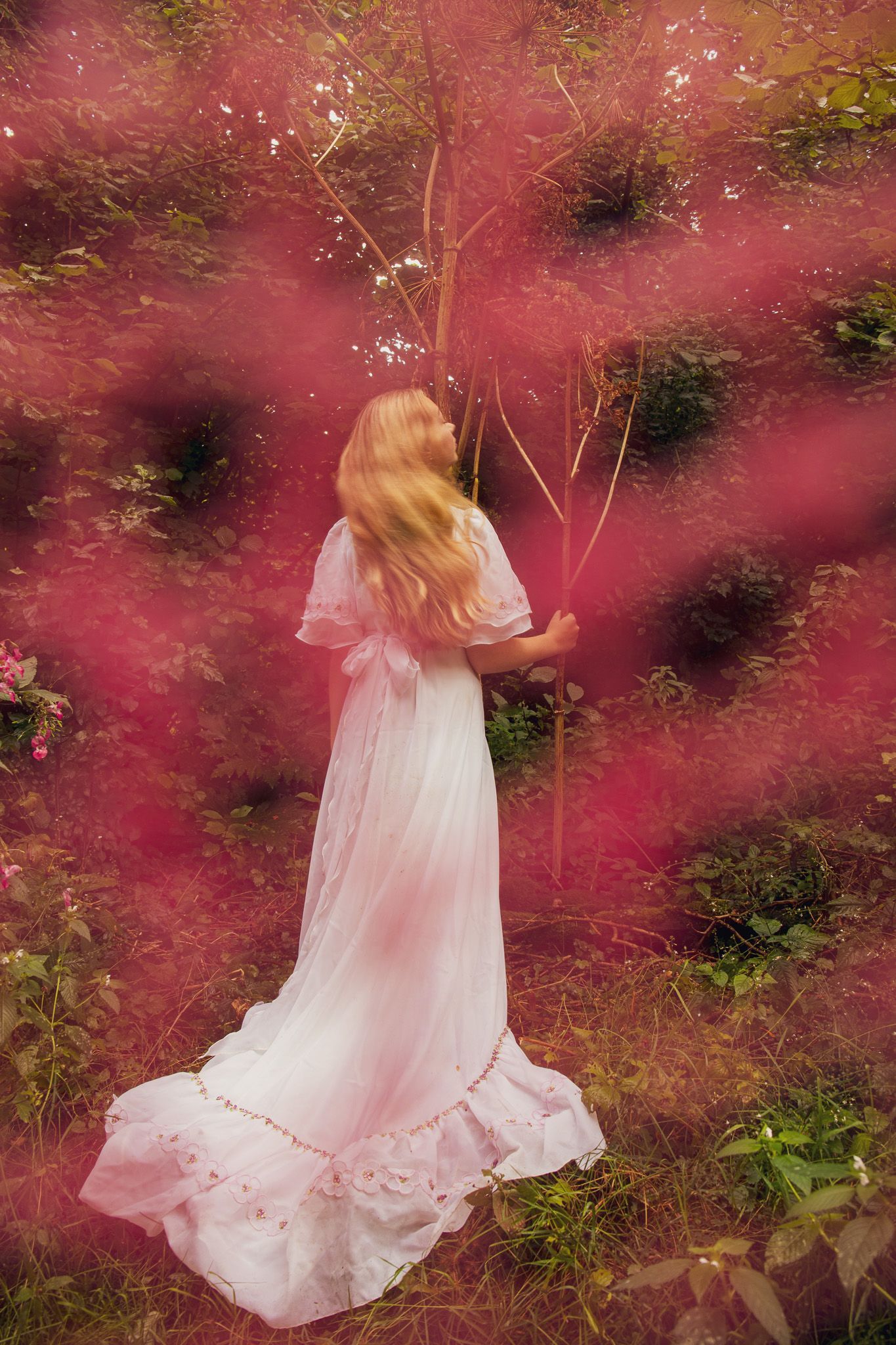 Vrouw in een zwierige witte jurk staat tussen roze bloesems in een tuin.