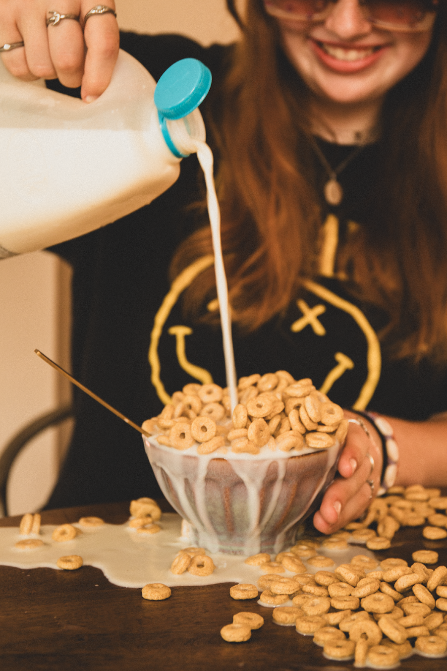 Melk wordt in een kom met ontbijtgranen op tafel gegoten, waarbij de stukjes ontbijtgranen eromheen verspreid liggen.