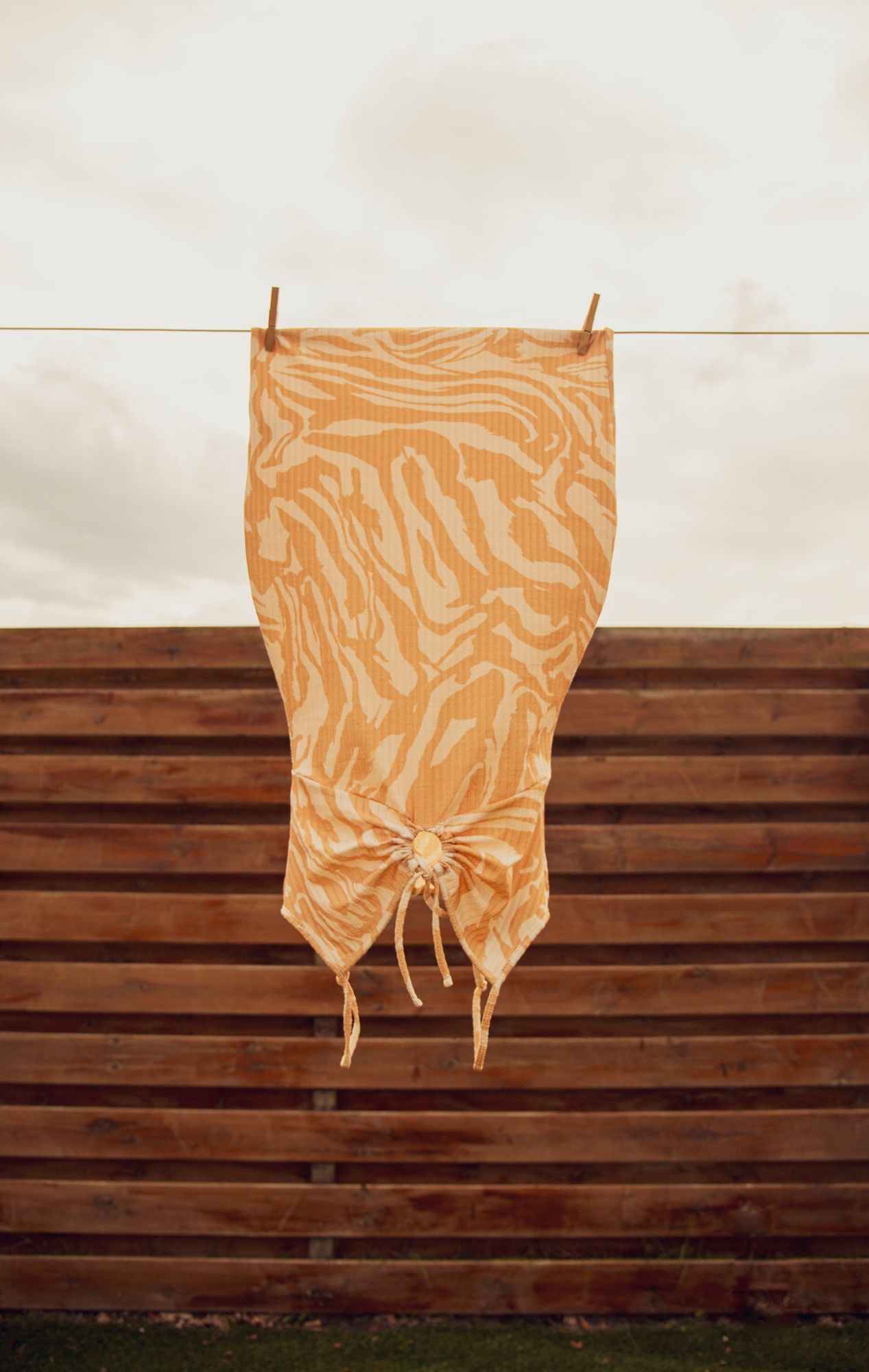 Een oranje, bedrukte doek hangt aan een waslijn boven een houten hek.