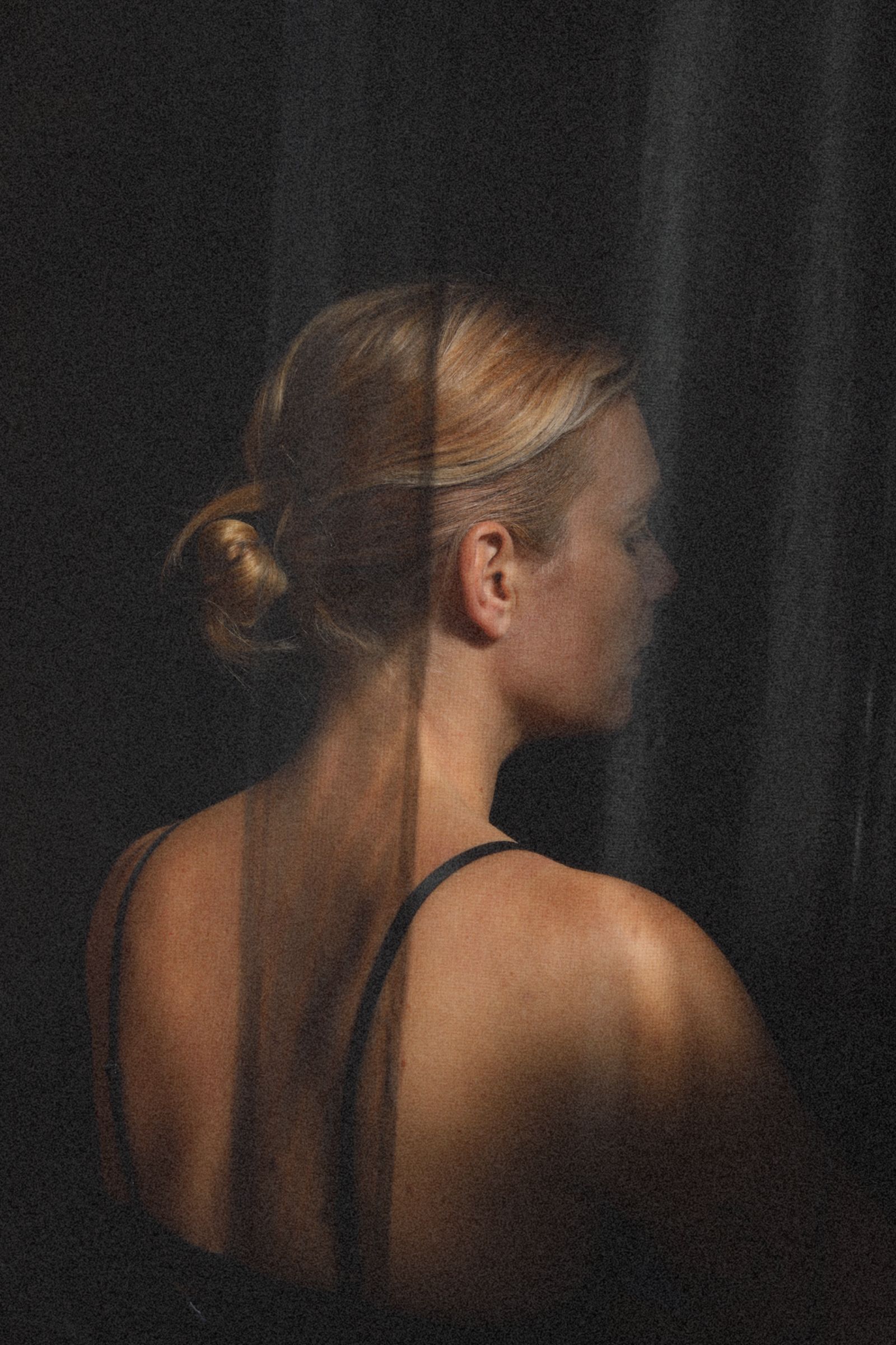 Portret van een blonde vrouw in profiel, staand tegen een donker gordijn, gekleed in een zwarte top.