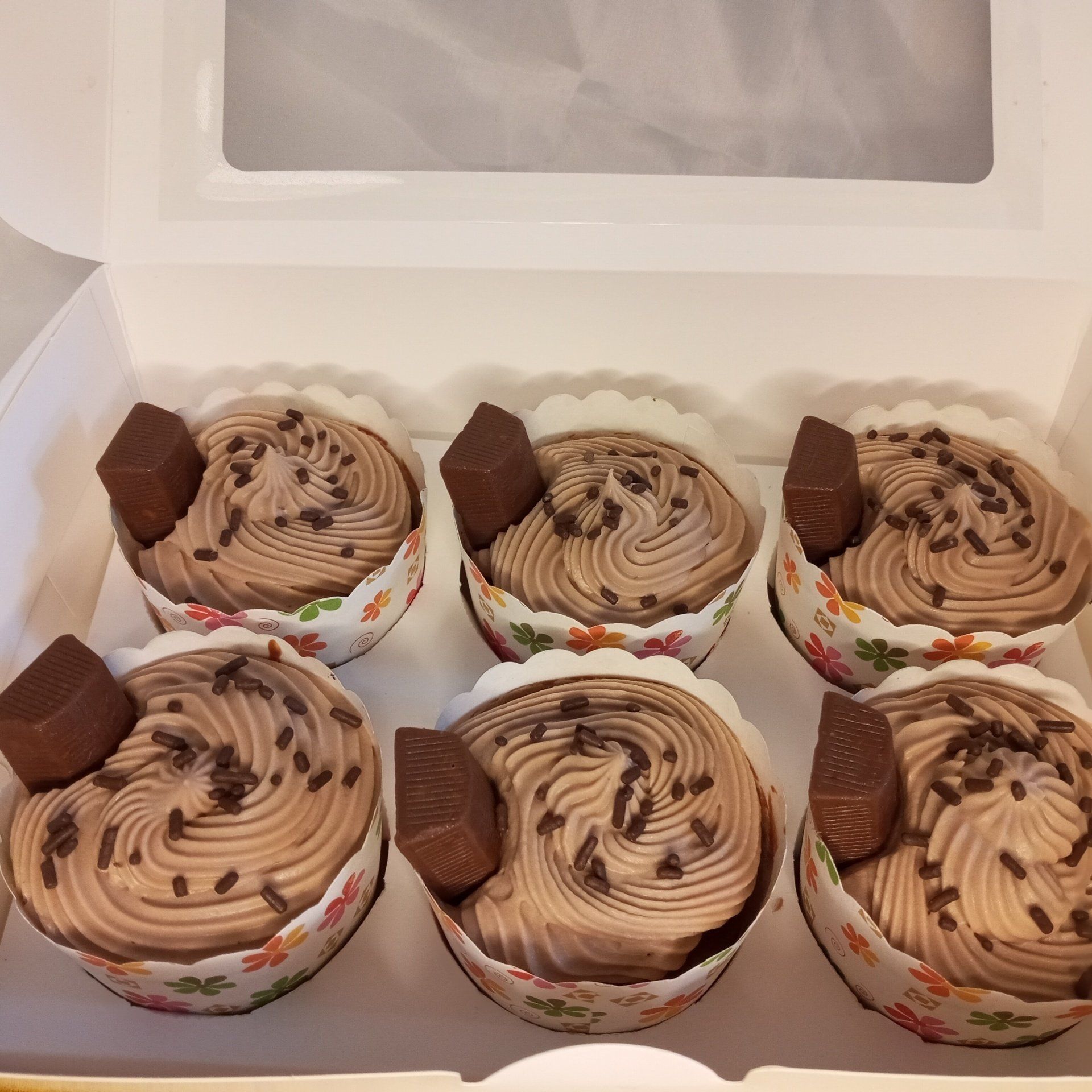 A box of chocolate cupcakes with frosting and chocolate sprinkles