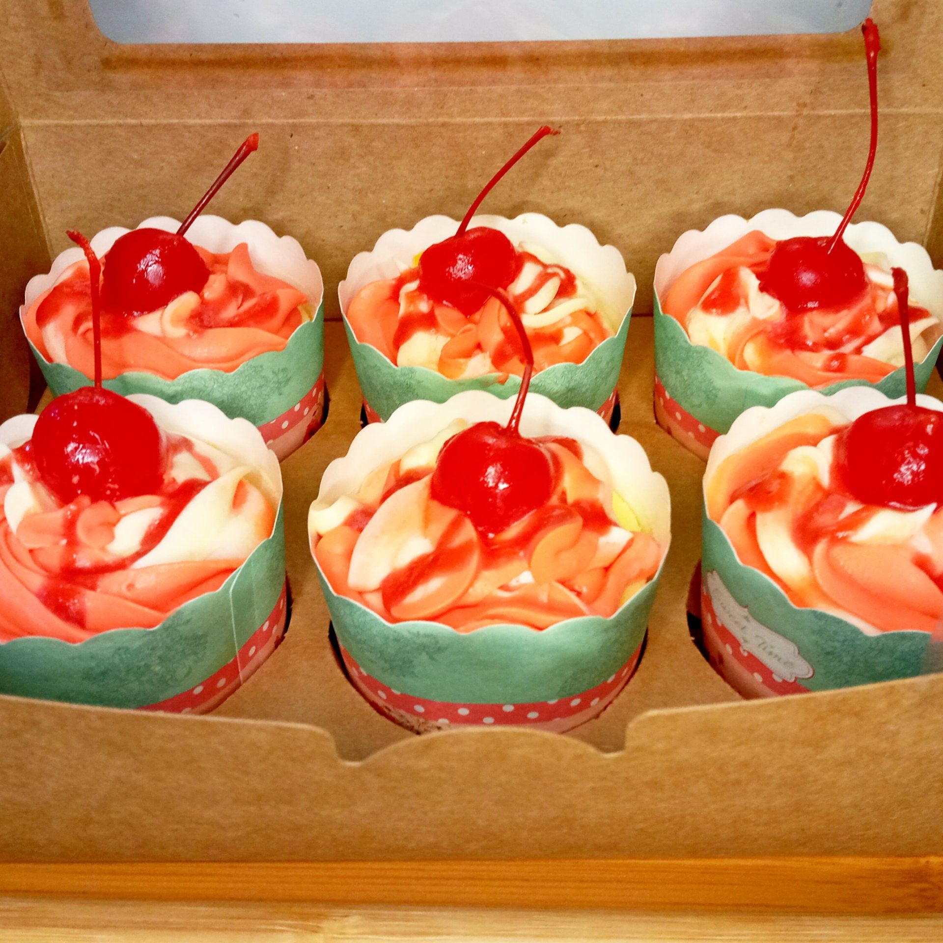 A box of cupcakes with a cherry on top