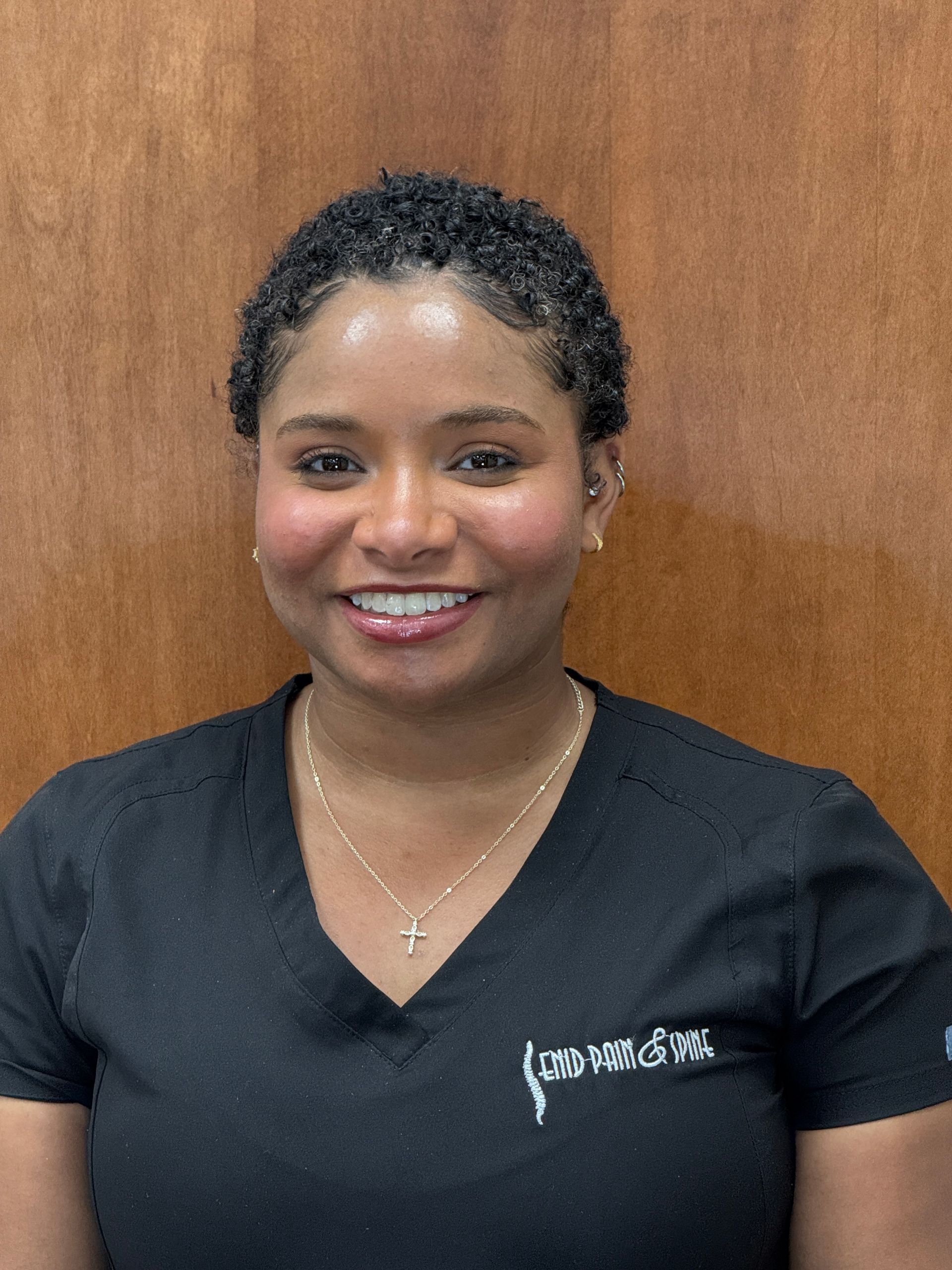 Woman with short curly hair, smiling, wearing a black top.