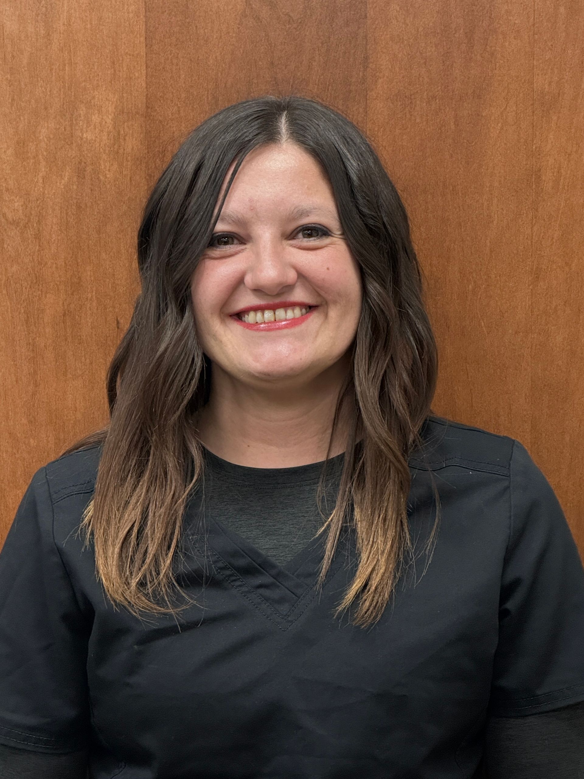 Woman with brown hair smiling, wearing a black top against a brown background.
