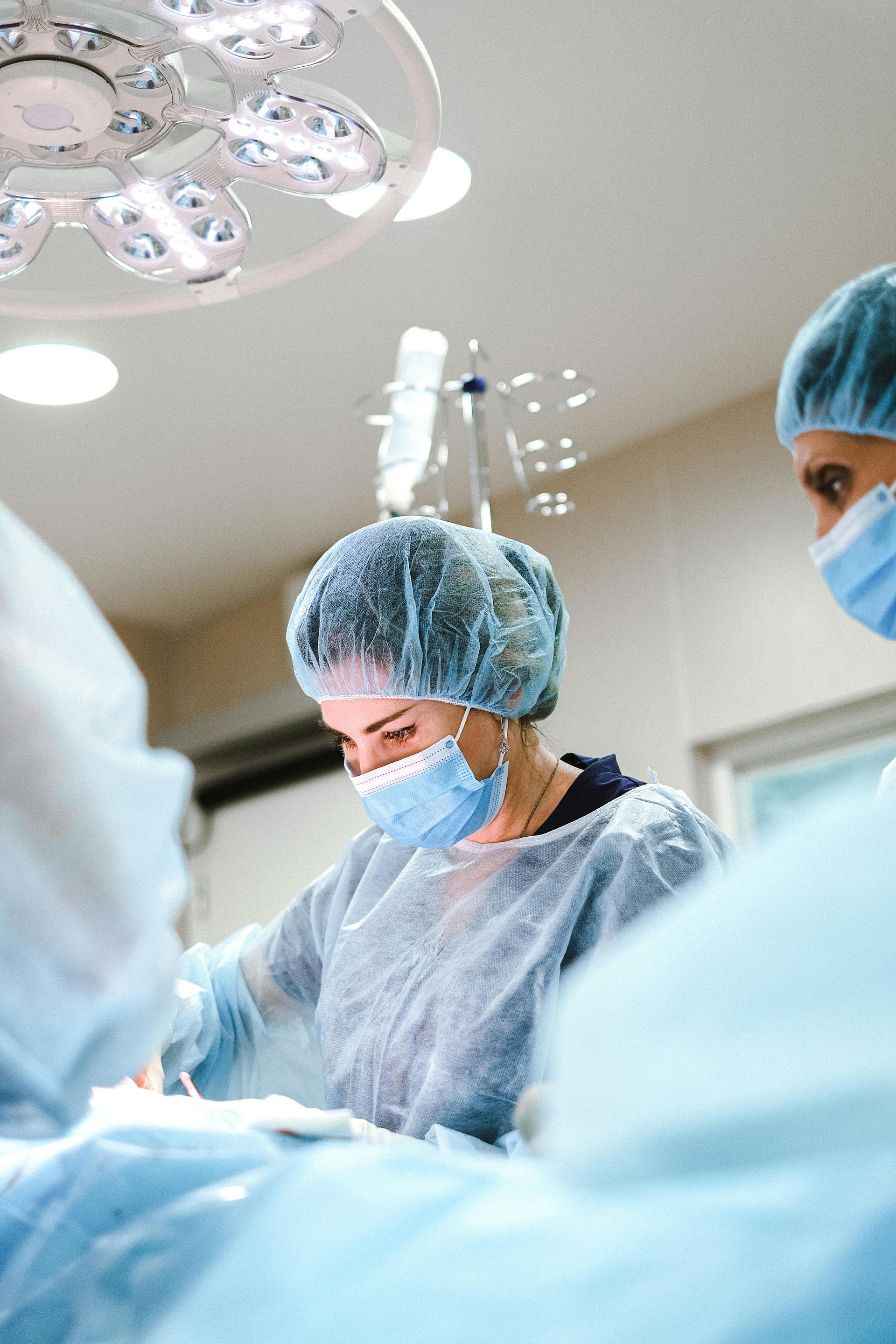 Surgeons in scrubs, masks, and caps operating under surgical lights in an operating room.