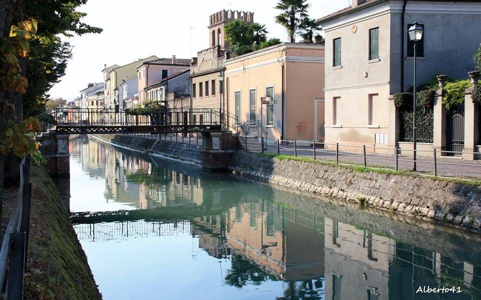 Canale in una città europea con edifici che costeggiano le rive; ponte; l'acqua riflette gli edifici e il cielo.