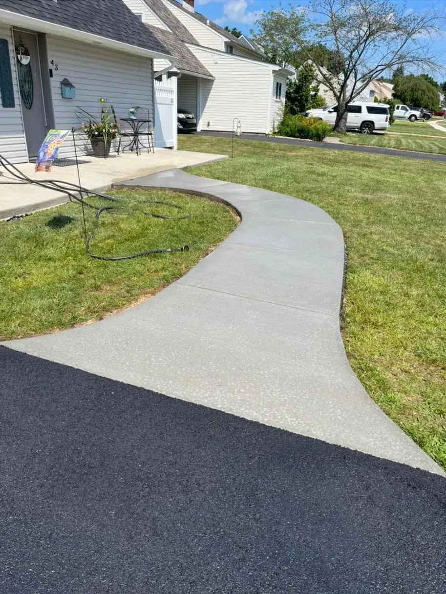 A new concrete walkway curves from a dark asphalt driveway toward the front porch of a suburban house. A new concrete walkway curves from a dark asphalt driveway toward the front porch of a suburban house.