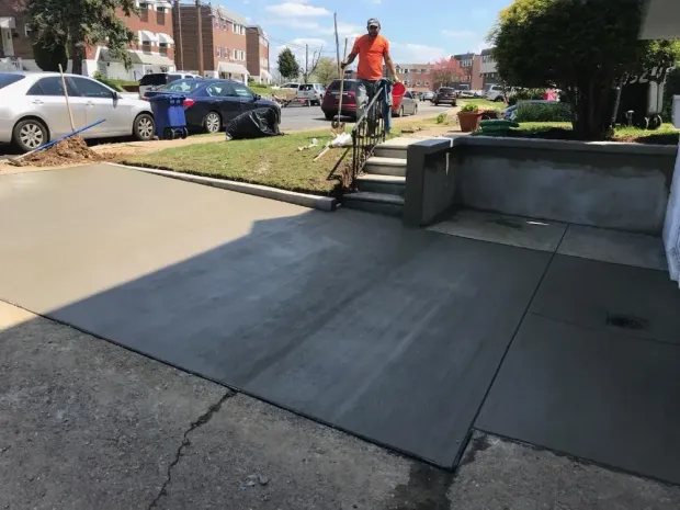 A worker in an orange shirt standing by newly poured concrete steps and a driveway on a sunny day. A worker in an orange shirt standing by newly poured concrete steps and a driveway on a sunny day.