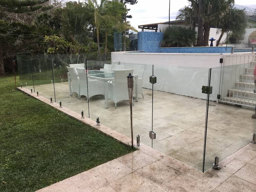 A Glass Fence Surrounds a Patio With a Pool in the Background — Riverside Aluminium & Stainless in Taree, NSW