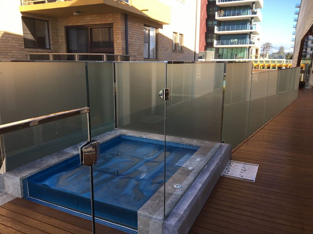 A Hot Tub is Surrounded by a Glass Fence on a Balcony — Riverside Aluminium & Stainless in Gloucester, NSW