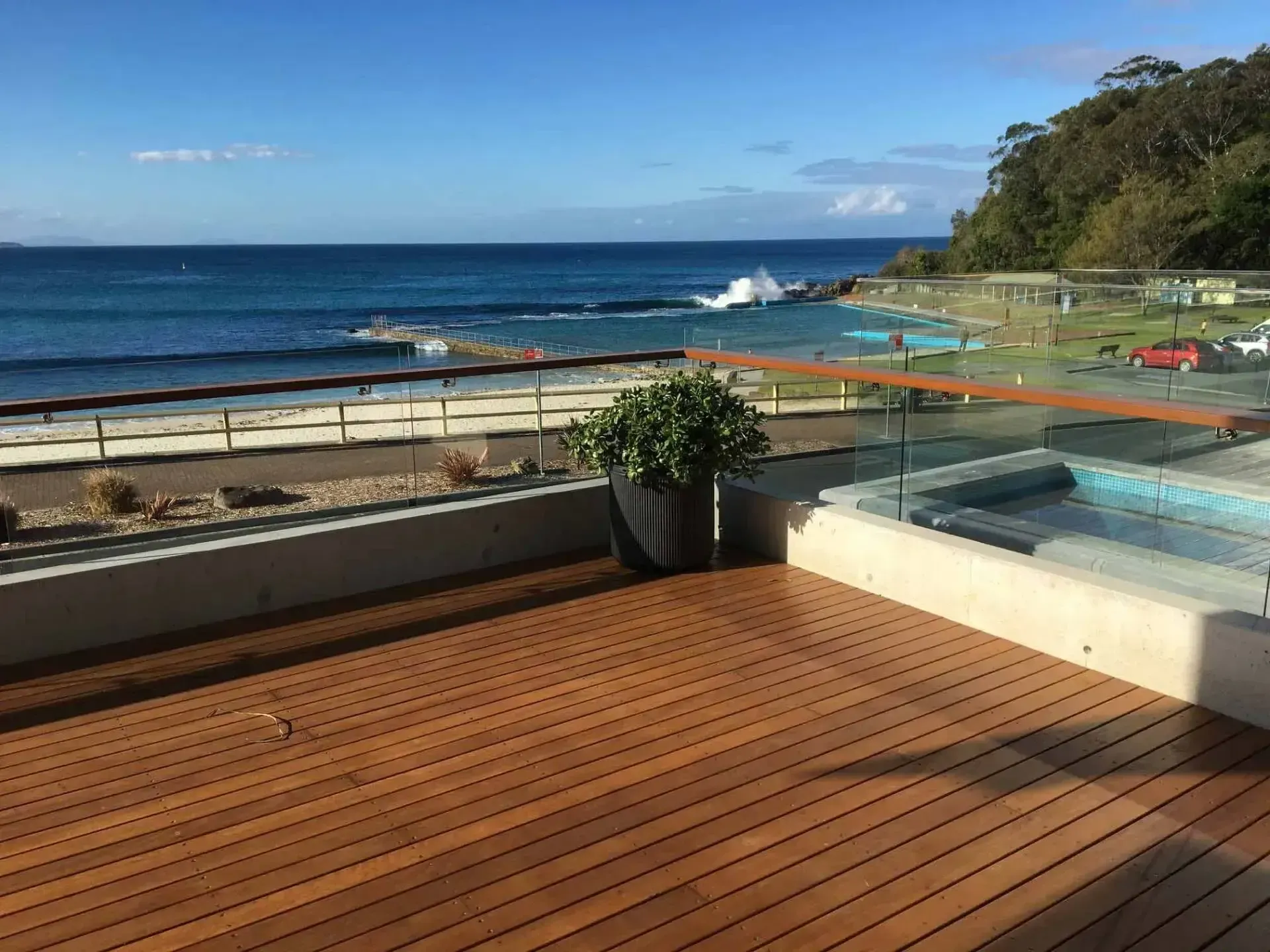 A Glass Fence Surrounds a Patio With a Pool in the Background — Riverside Aluminium & Stainless in Gloucester, NSW