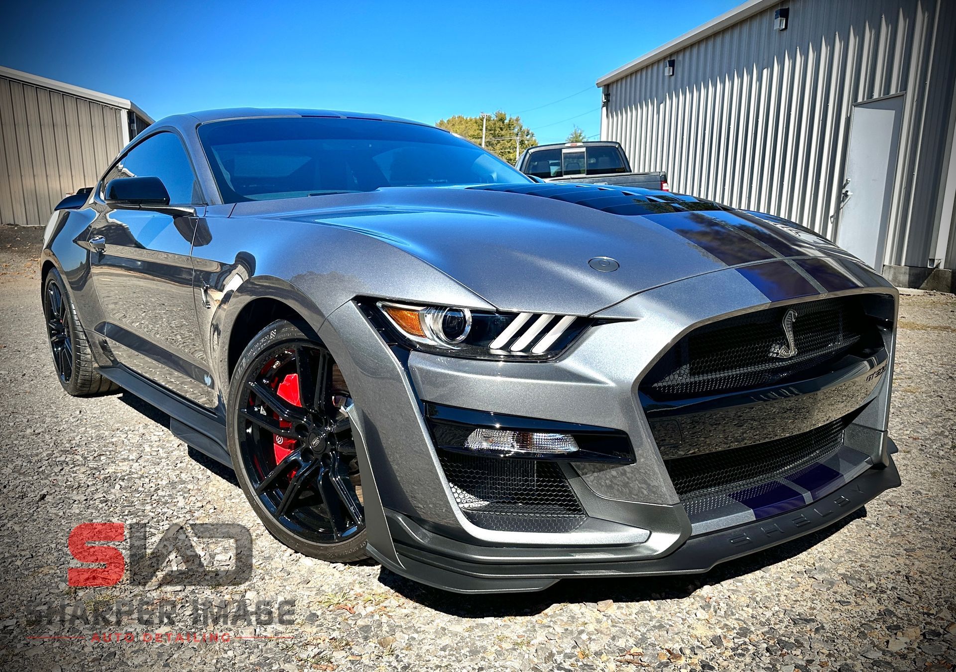 Gray Shelby GT500 with blue stripes and red brake calipers parked in front of a building.