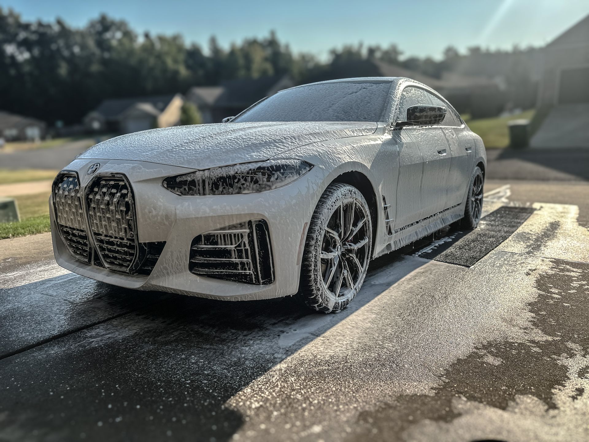 A white BMW sedan covered in white soap suds being washed outside.