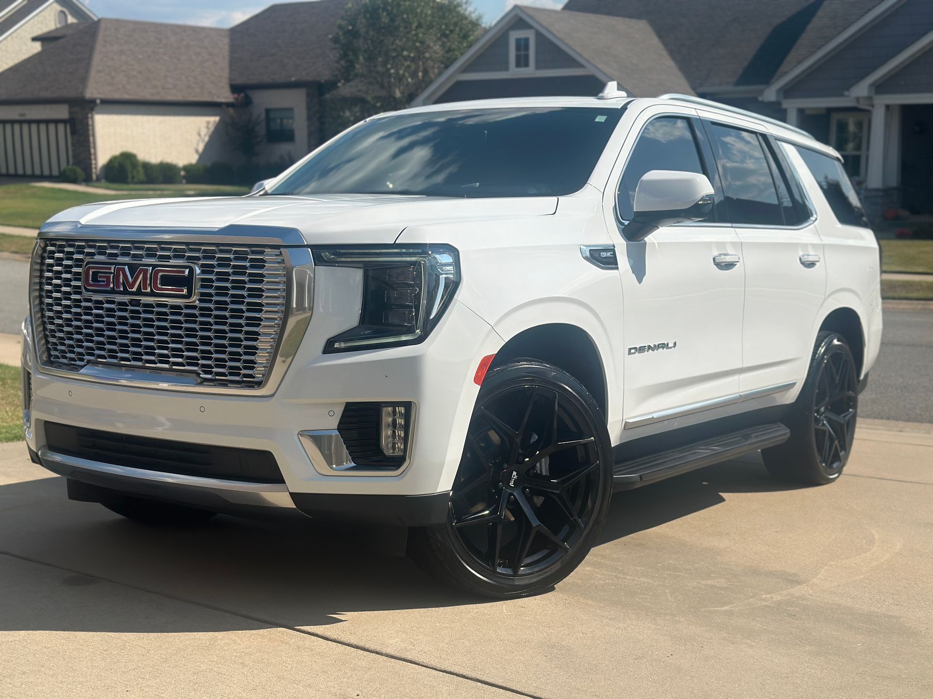 White GMC Yukon Denali SUV with black wheels parked on a driveway in front of a house.