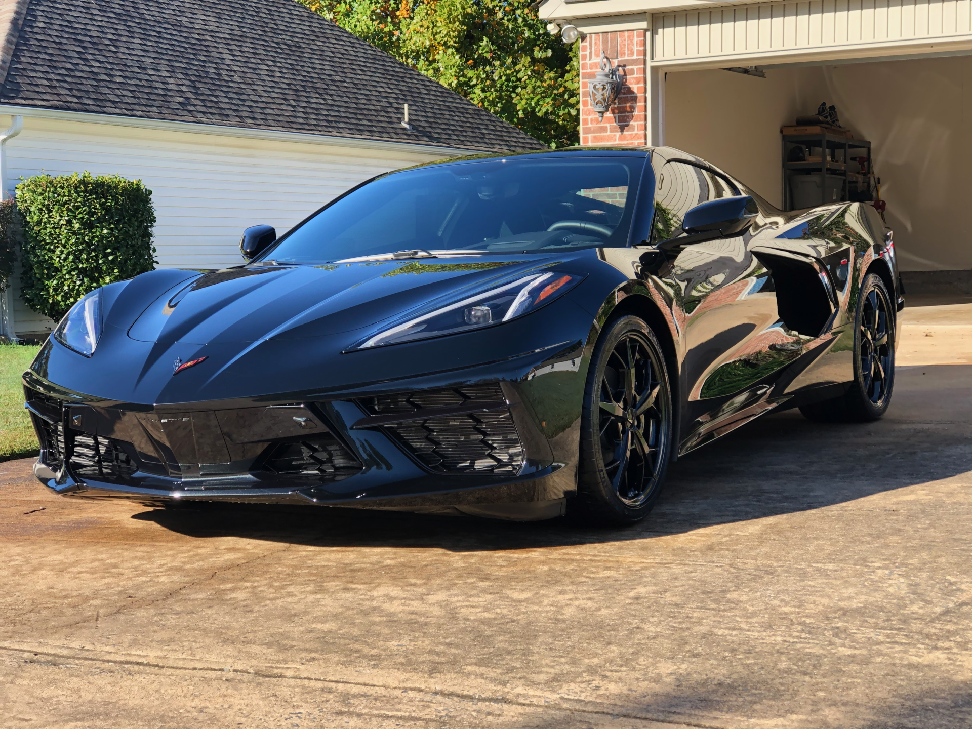 Black Corvette sports car parked in a driveway in front of a garage.