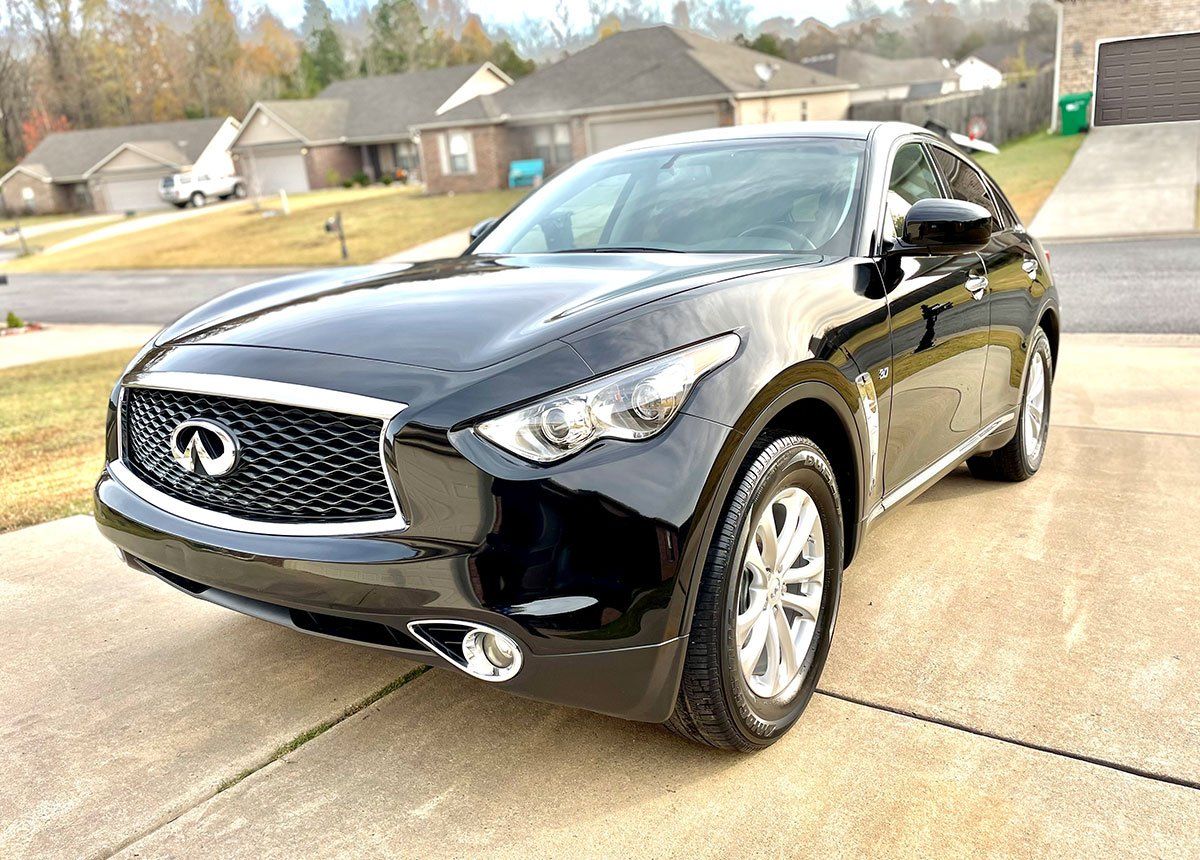 Black Infiniti FX SUV parked on a driveway in front of a suburban house.