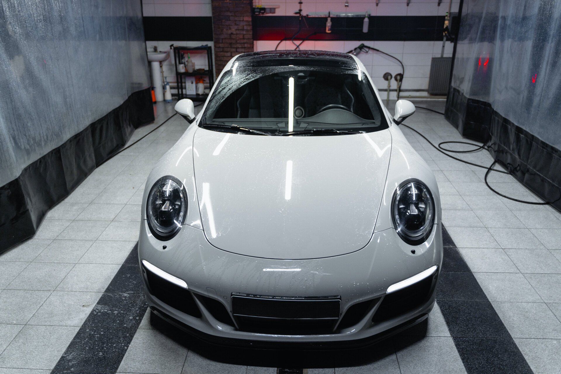 White Porsche sports car inside a garage, reflecting overhead lights.