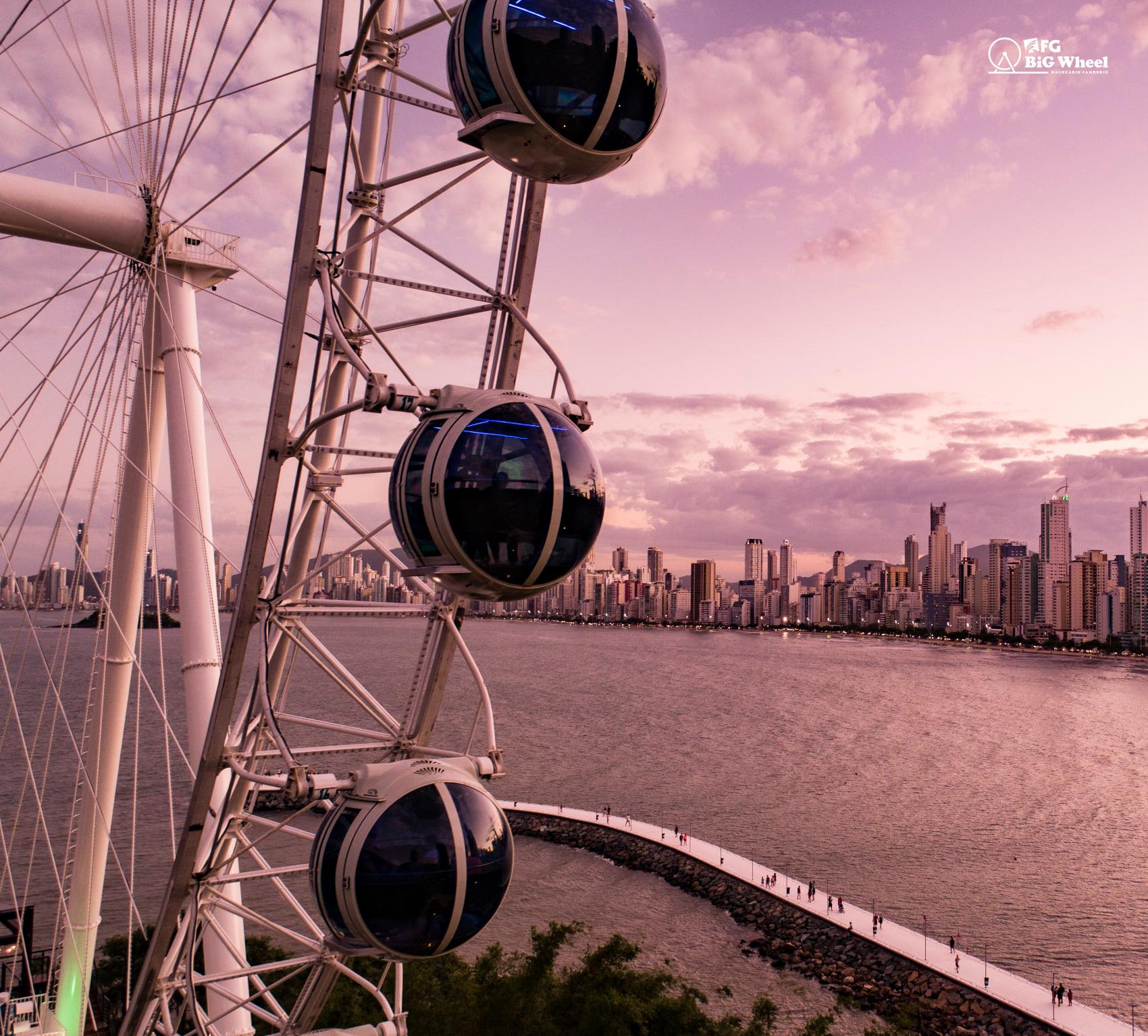 Roda gigante com gôndolas com vista para o horizonte da cidade e para a água ao anoitecer.